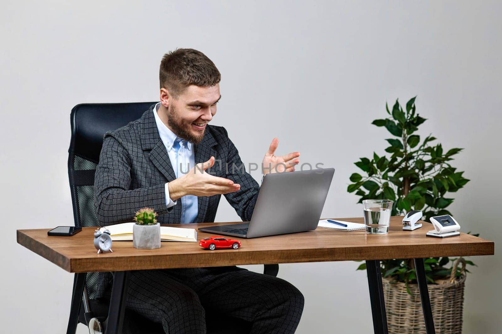 young friendly man talking at laptop webcam, sitting on chair at desk, using laptop pc computer