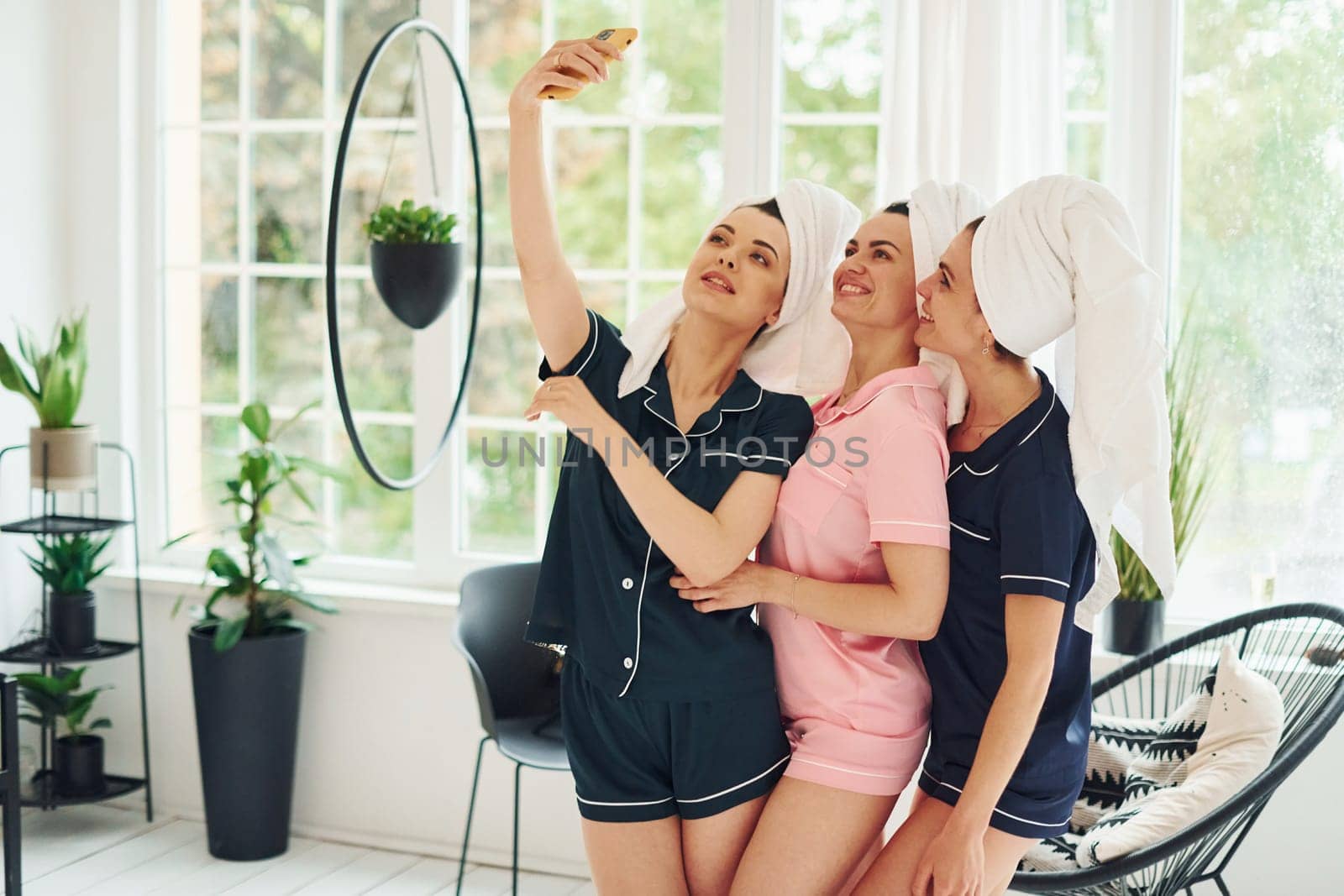 Cheerful young women in pajamas having fun indoors at daytime together.