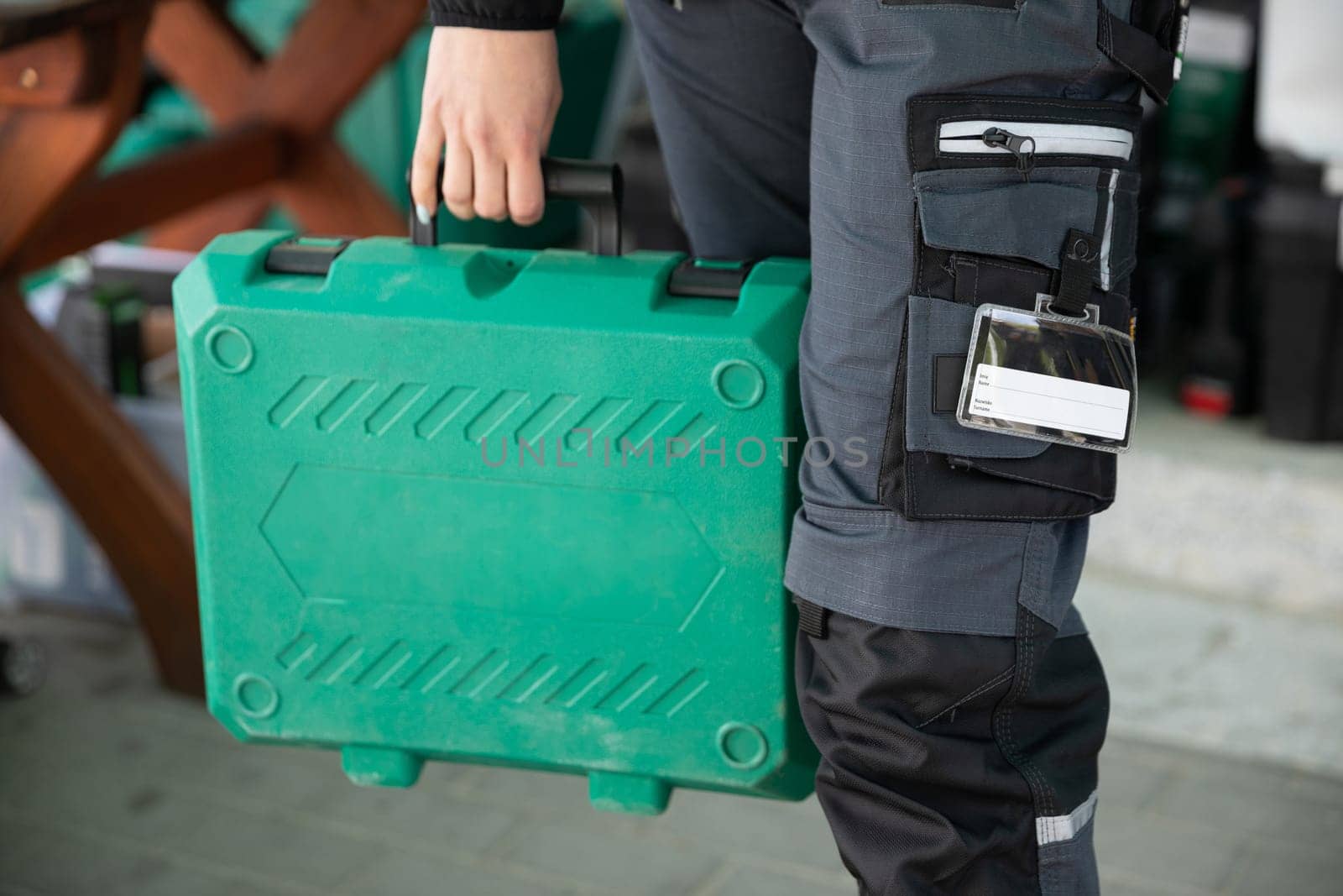 A close-up view of a woman dressed in work clothes holding a plastic green tool case.