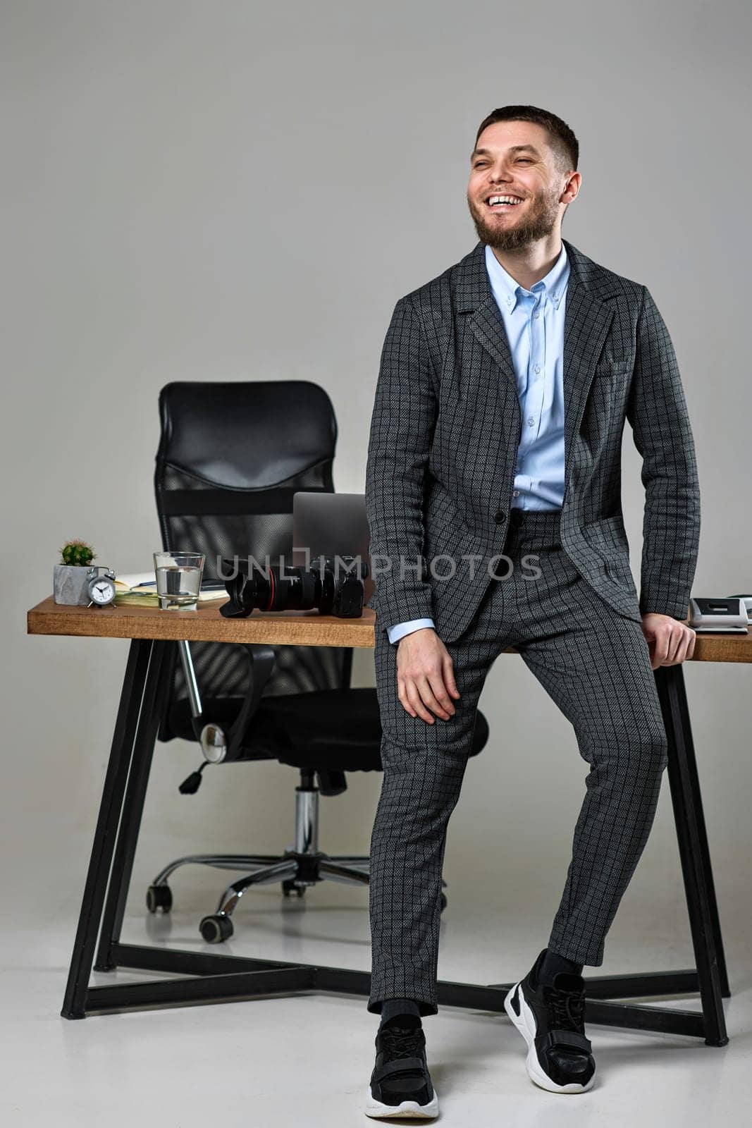 bearded male photographer smiling cheerfully while working at her desk.