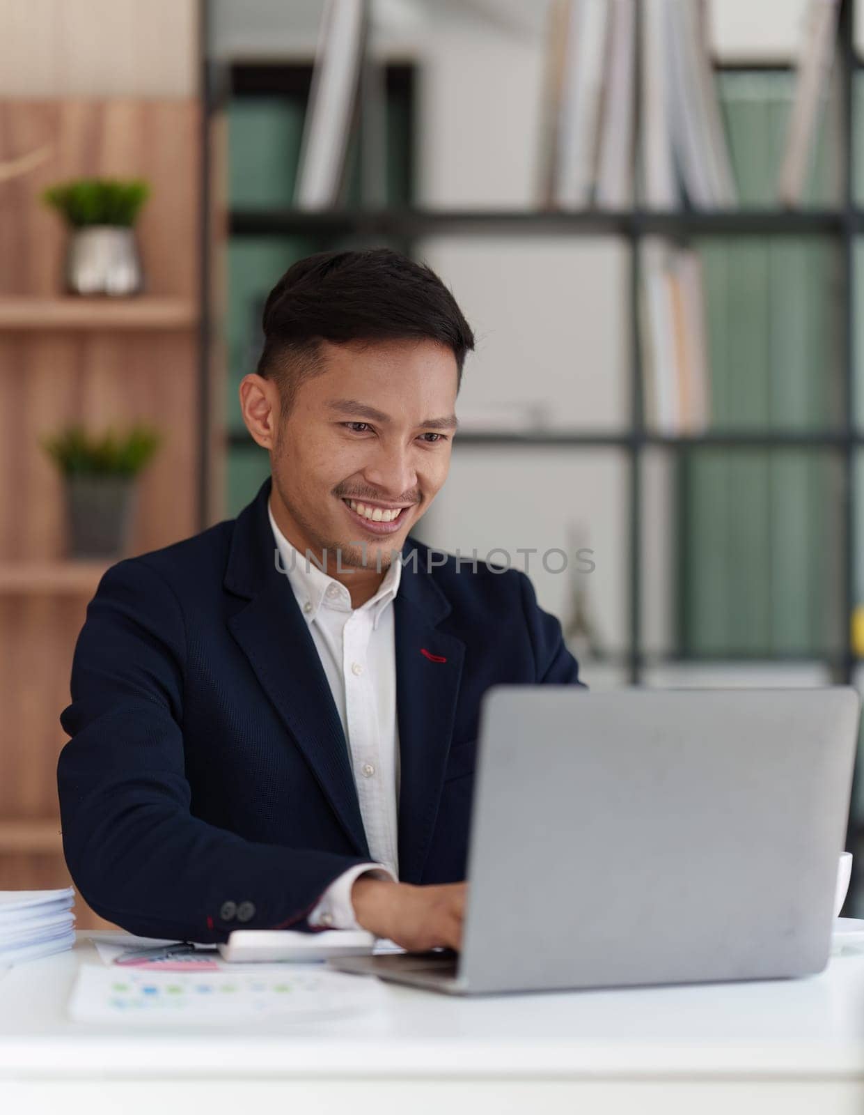 Smiling Asian Banker makes financial report and studies annual figures, analyzes profits. Accountant checks status of financial.