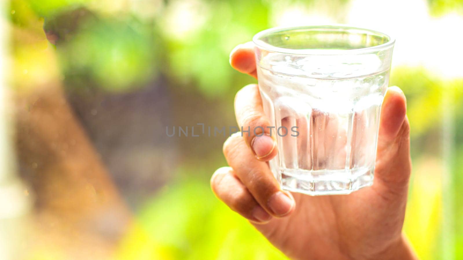 hand holds clear water in glass . hand holding A clear glass of clean mineral water . Concept of environment protection, healthy drink. nature blurred background