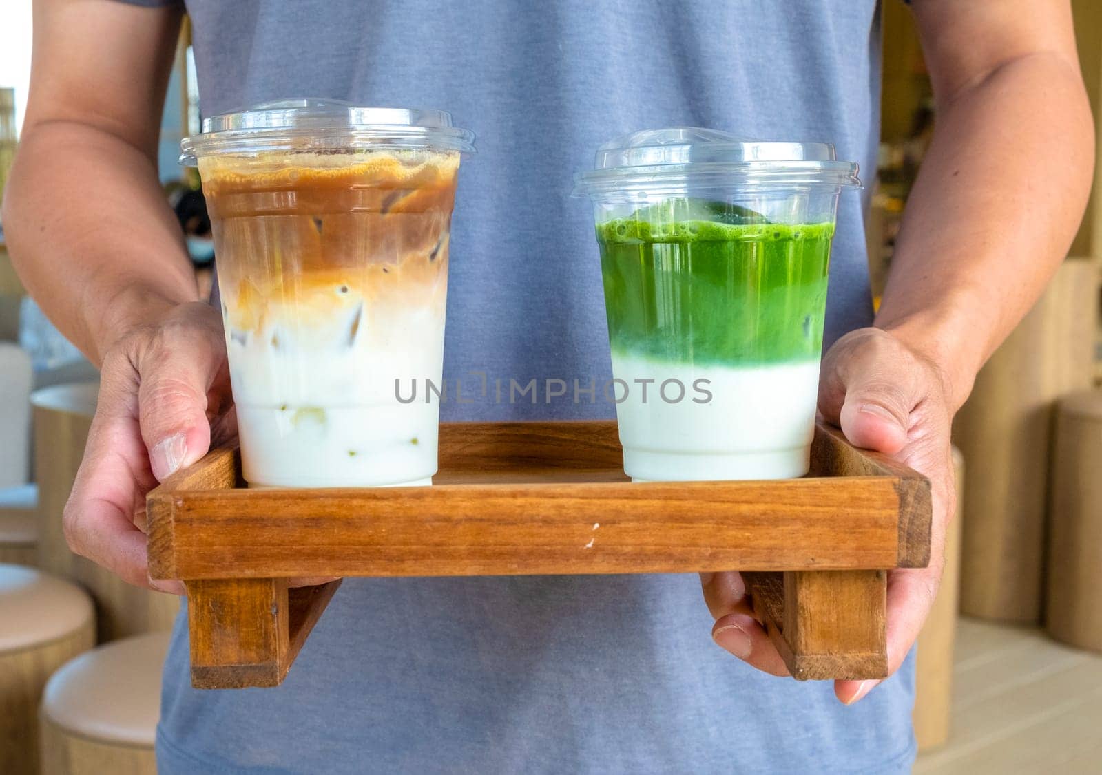 A man is holding a ice latte coffee and matcha latte on wooden plate