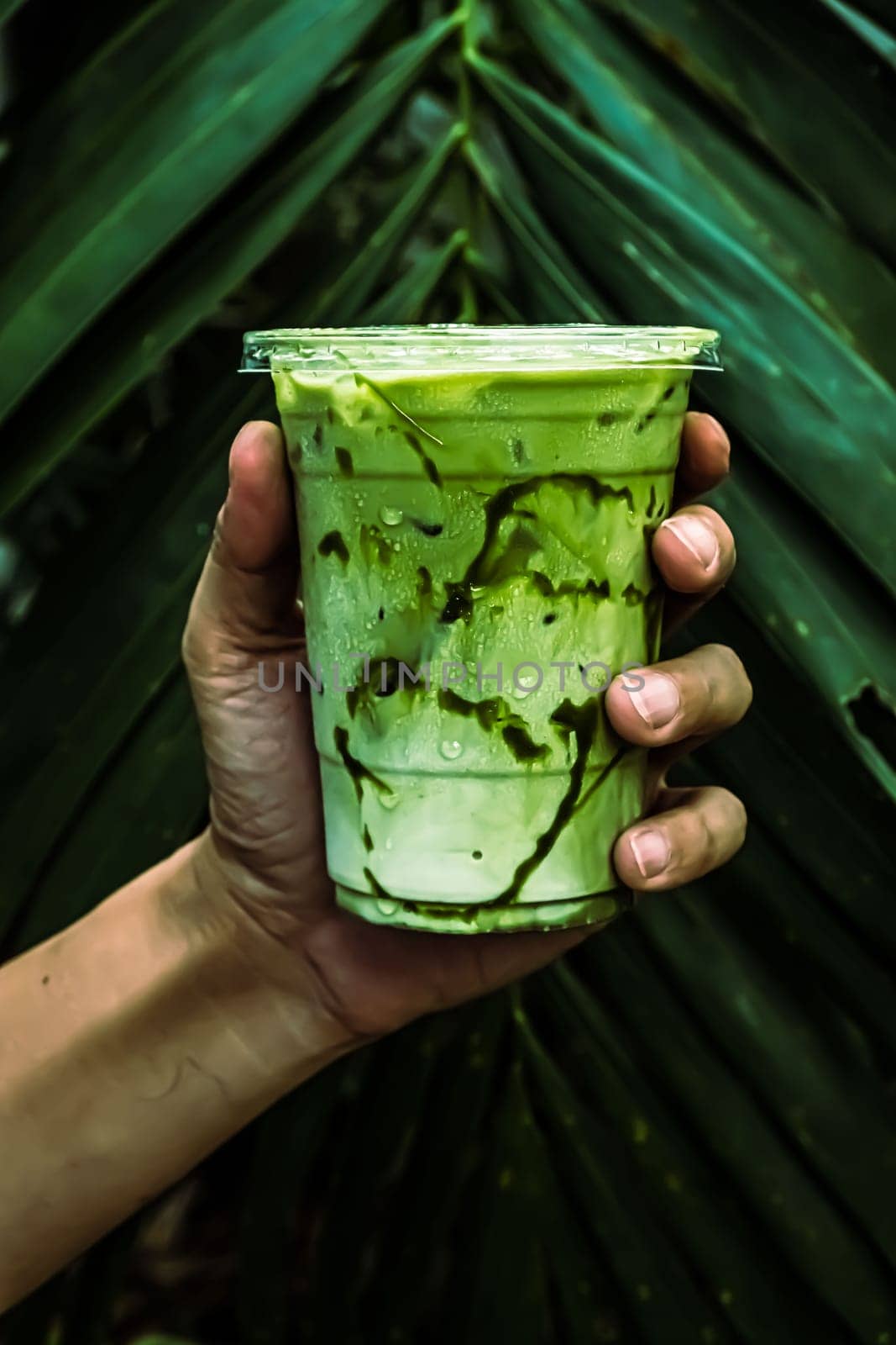 iced Green matcha tea mixed with ice cube and milk in latte glass  with green nature background
