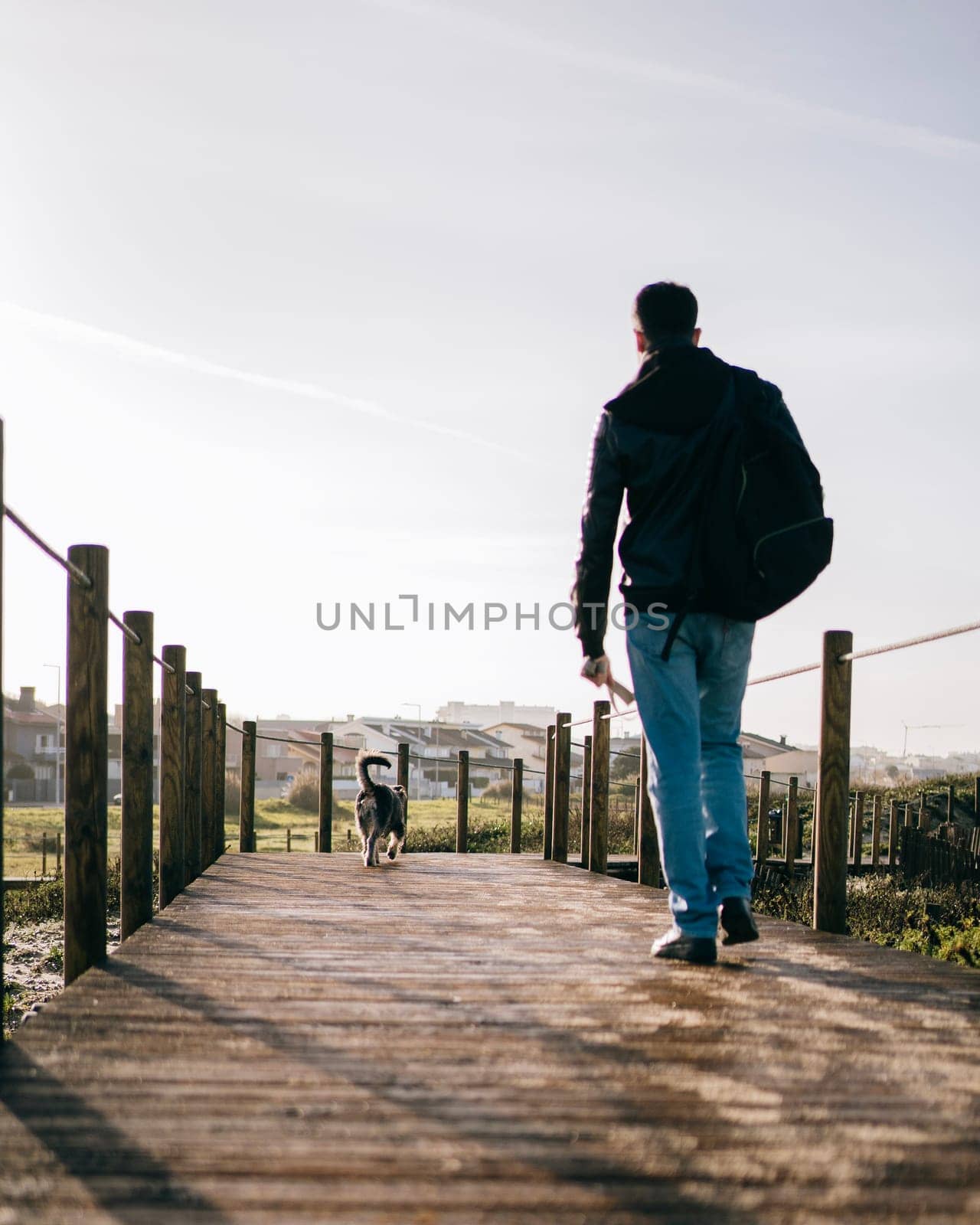 Low angle view of man with backpack on morning walk with his dog through a wooden path.