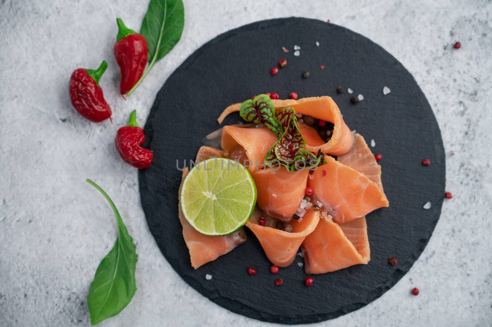 Fresh smoked salmon slices with peppers, greens and lime on concrete background