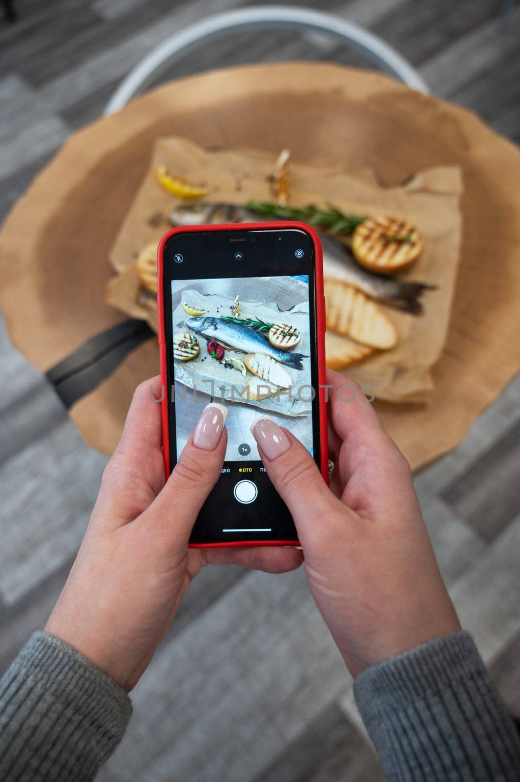 Woman takes photo of sibas fish with greens and vegetables. On a wooden background.