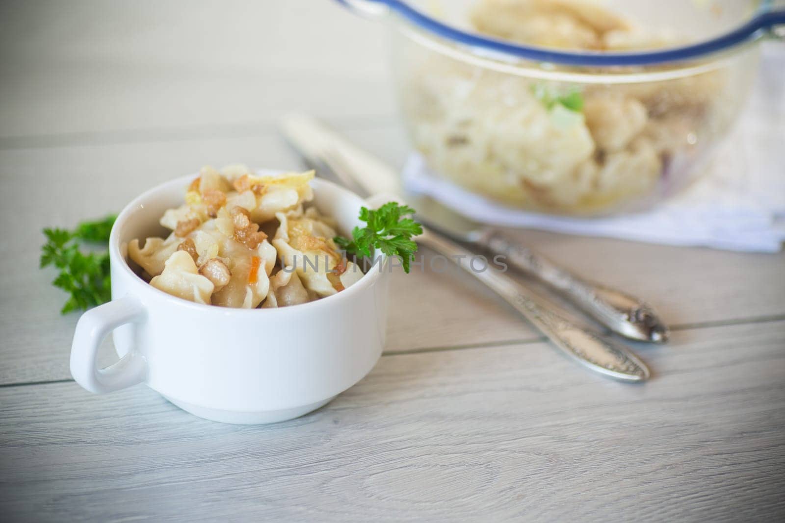 cooked dumplings with potatoes and fried onions, in a bowl on a wooden table.