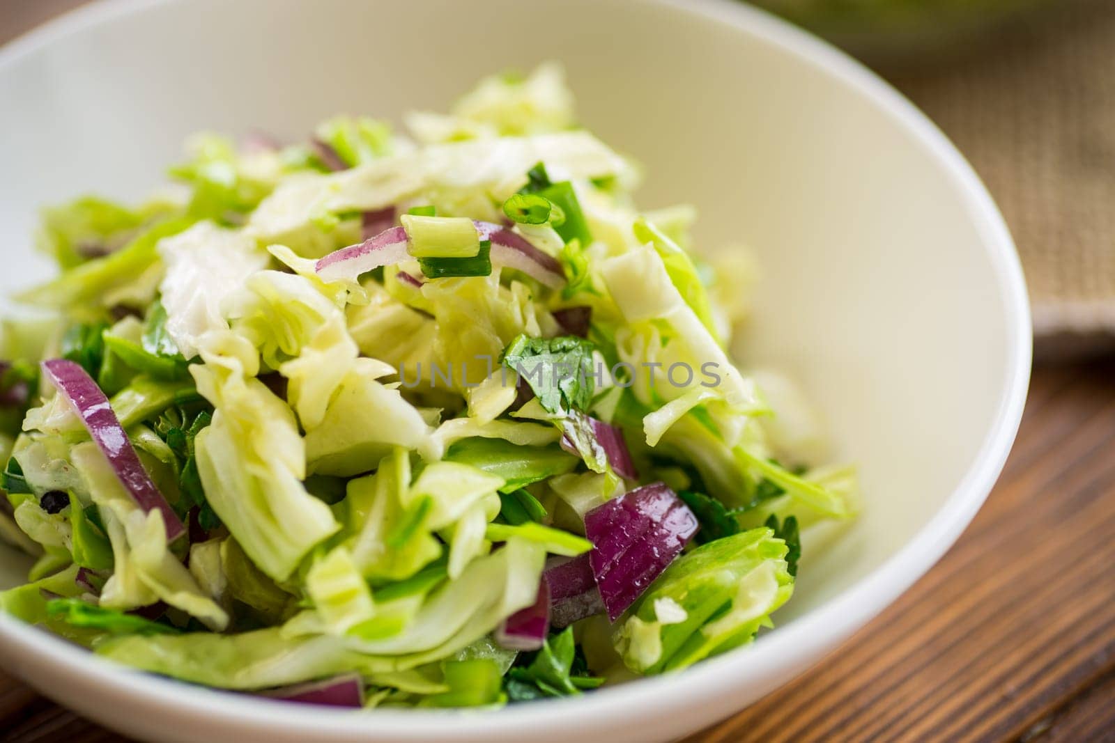 Young cabbage salad with purple onions in a bowl on a wooden table.