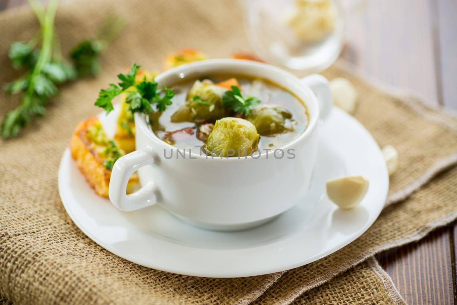 Hot cooked soup with Brussels sprouts, vegetables and croutons, in a plate on a wooden table.