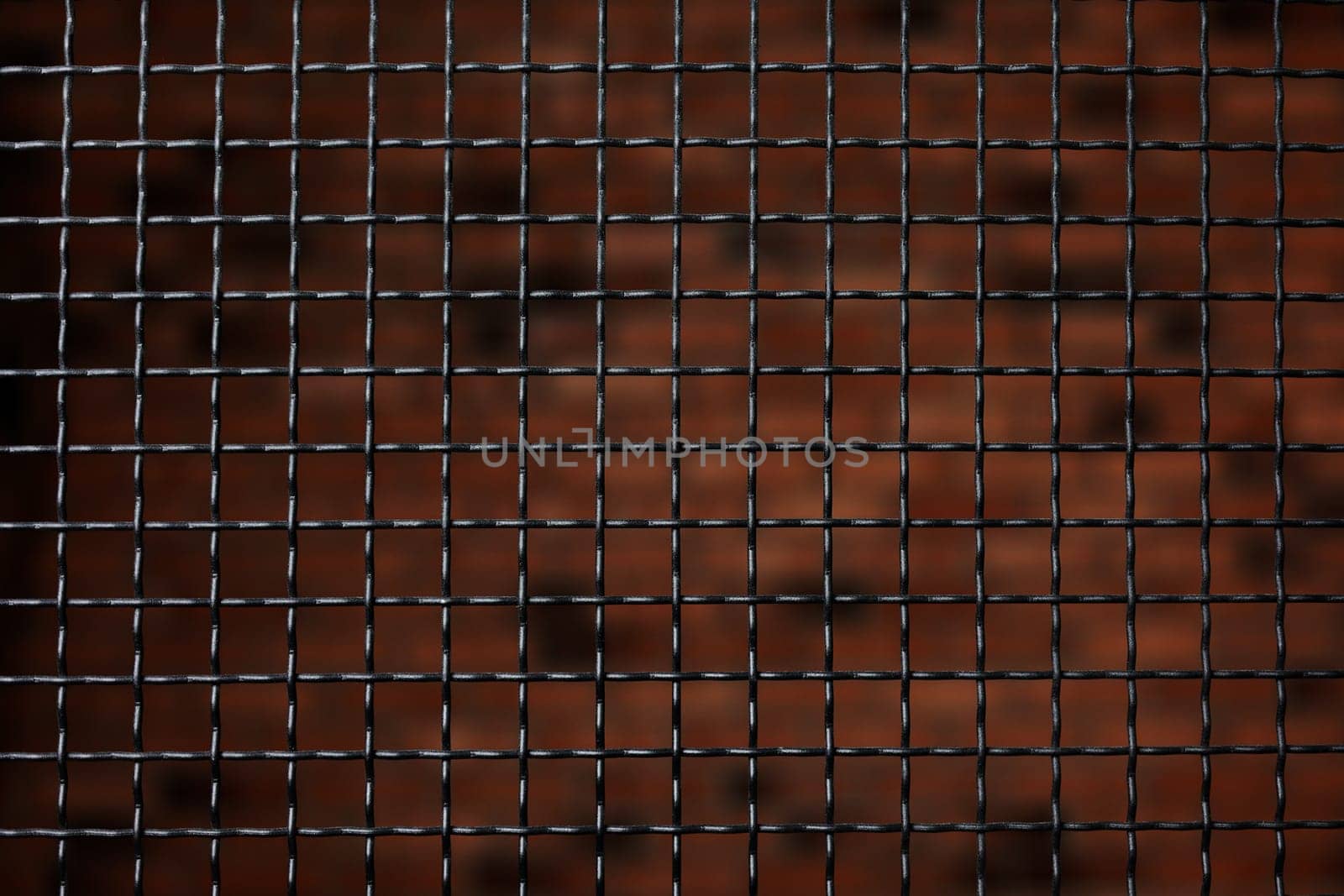 Black metal grating on natural brick background, steel fence indoors close up. Wallpaper metallic wire barrier. Stylized design solution in the interior. Security and safety concept.