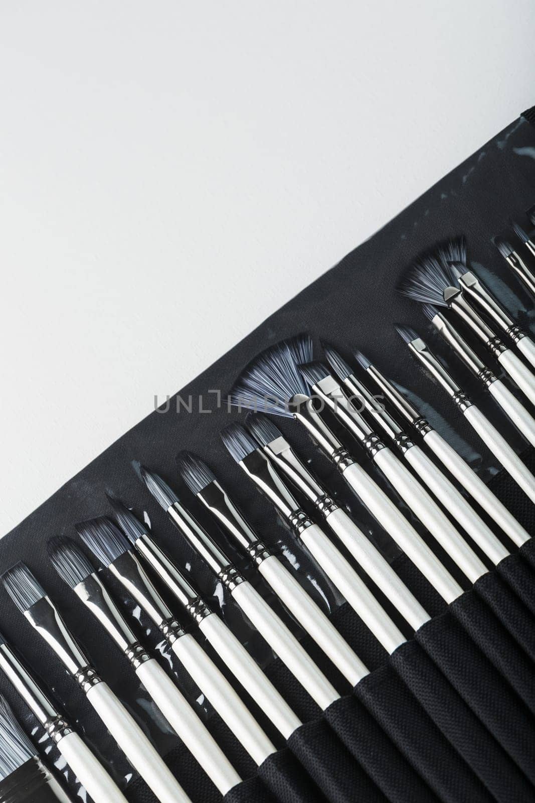 Brushes, palette knives in a pencil case on a white canvas background by AlexGrec