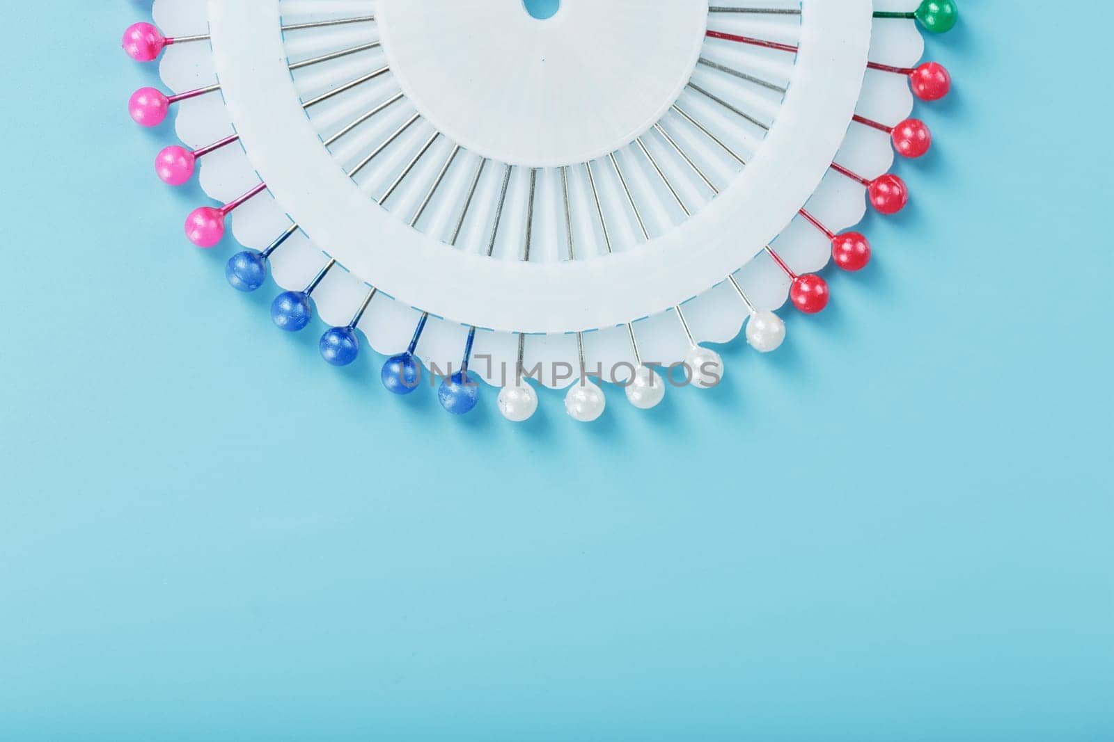 Sewing mother-of-pearl pins in a round white package on a blue background with free space