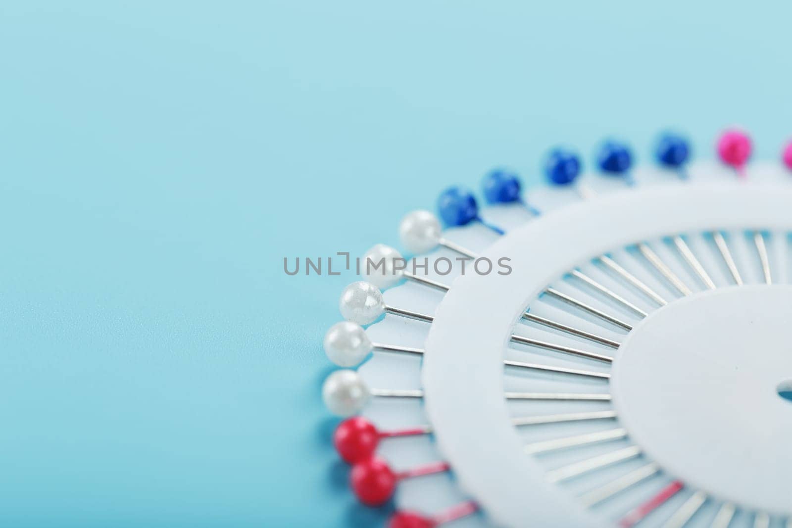 A set of multicolored needles pins in a round platform on a blue background with free space