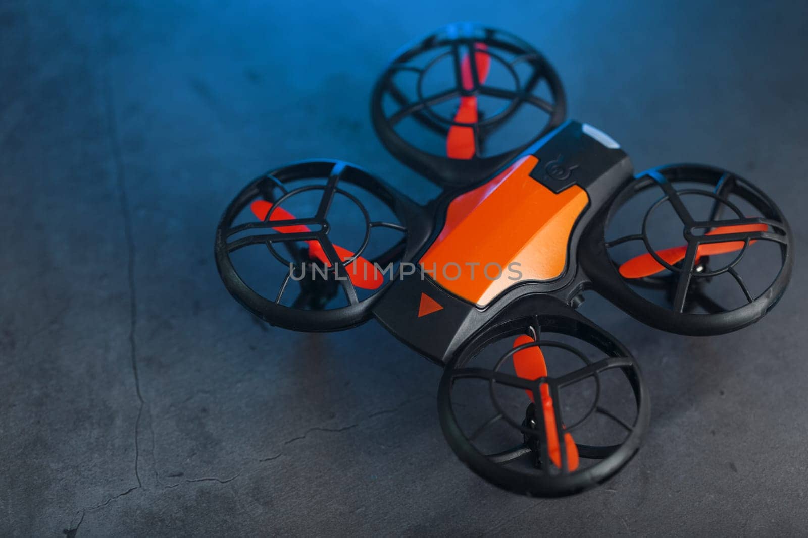 A reconnaissance quadcopter drone with an orange body and blue LED backlight on a dark background
