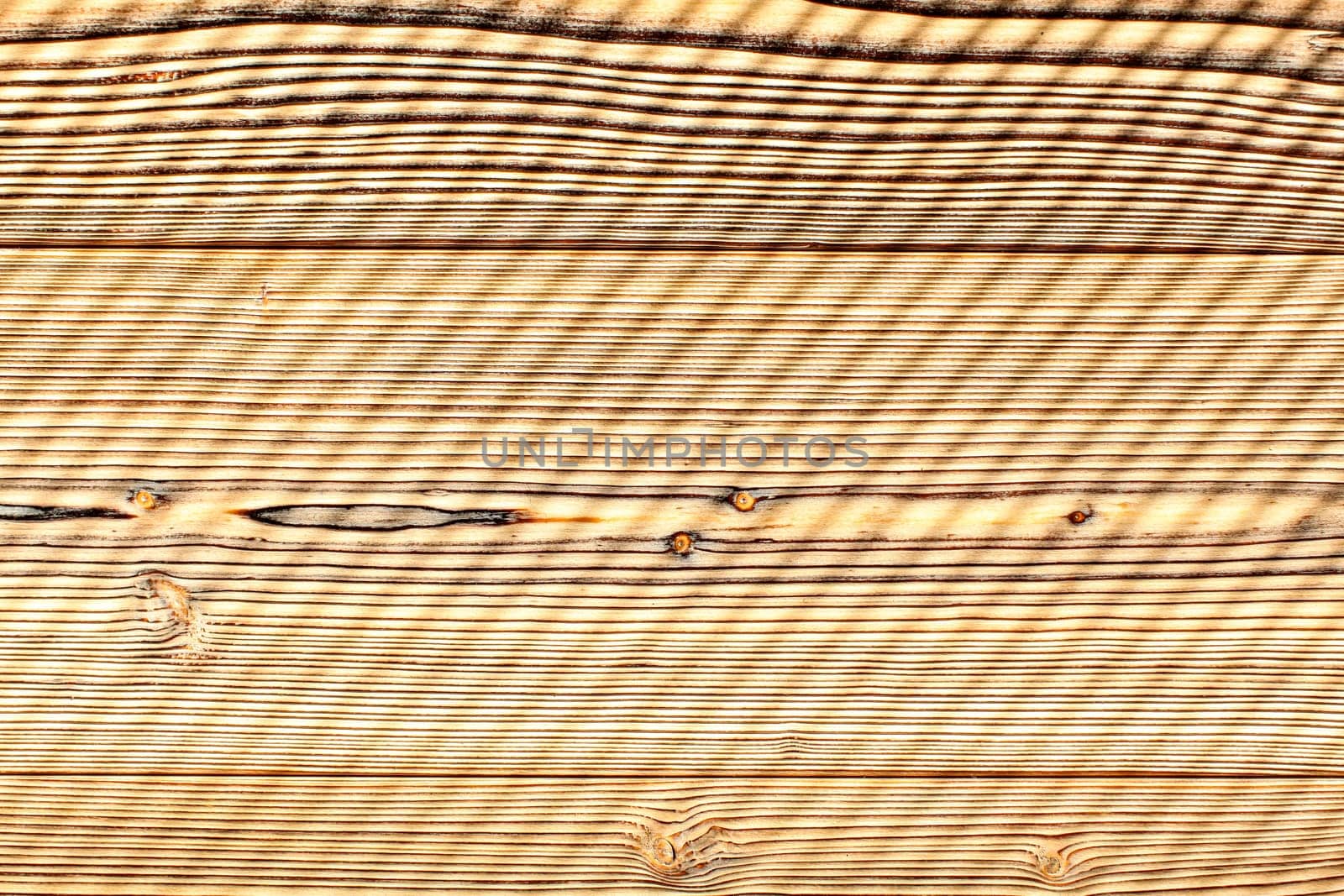 Top view - desk made from wooden boards lit by morning sun, shades leaving diagonal stripes pattern. Abstract wooden background.