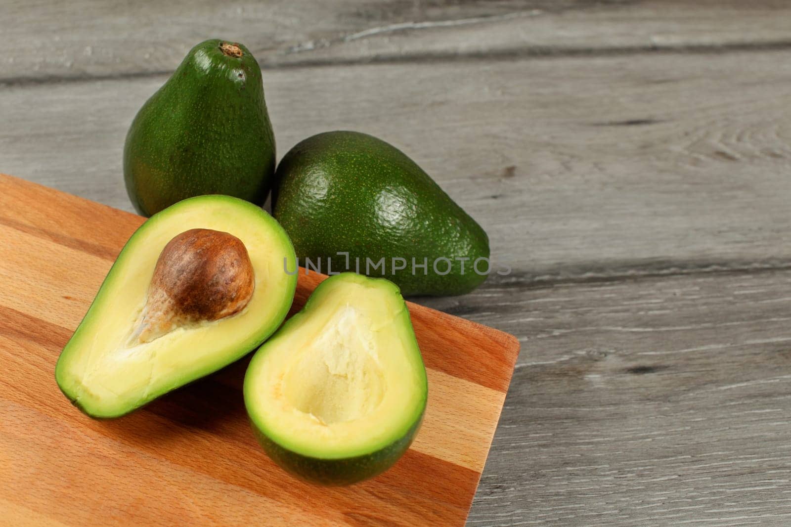 Avocado cut in half brown seed visible, wooden chopping board under, two whole green pears next to it.