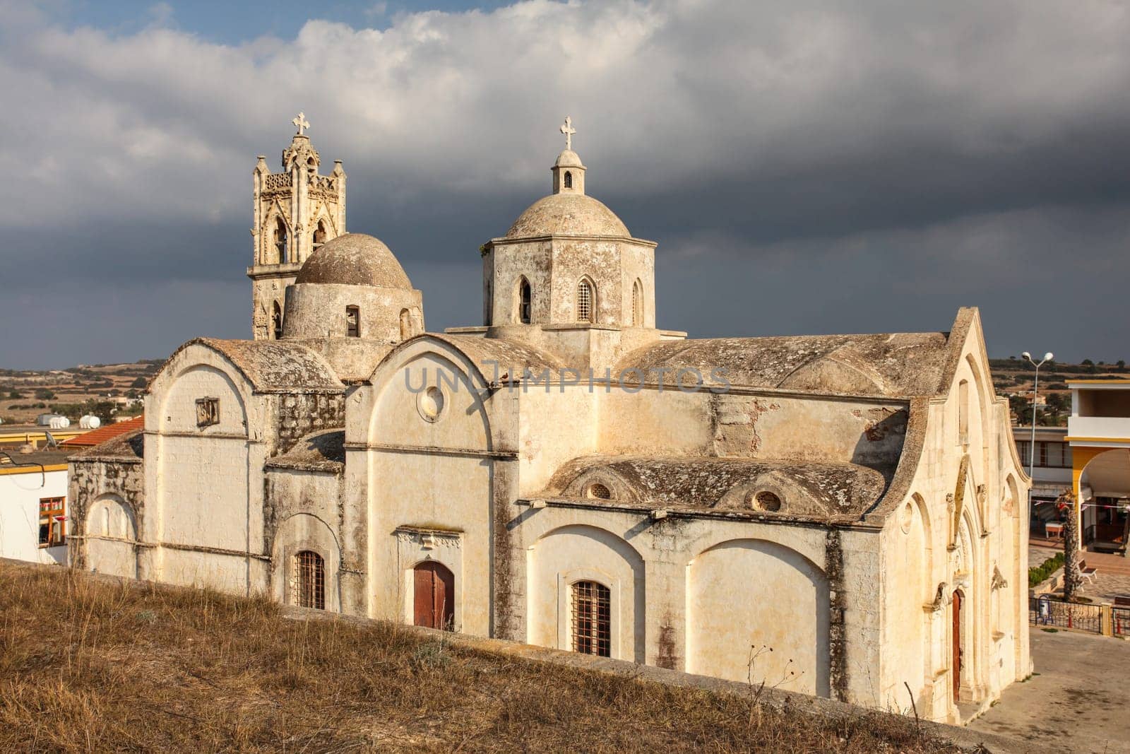 Ayios Synesios Church in Rizokarpaso (Dipkarpaz), lit by afternoon sun, some heavy clouds in background. This northern Cyprus town is known for Christians and Muslims living in harmony.