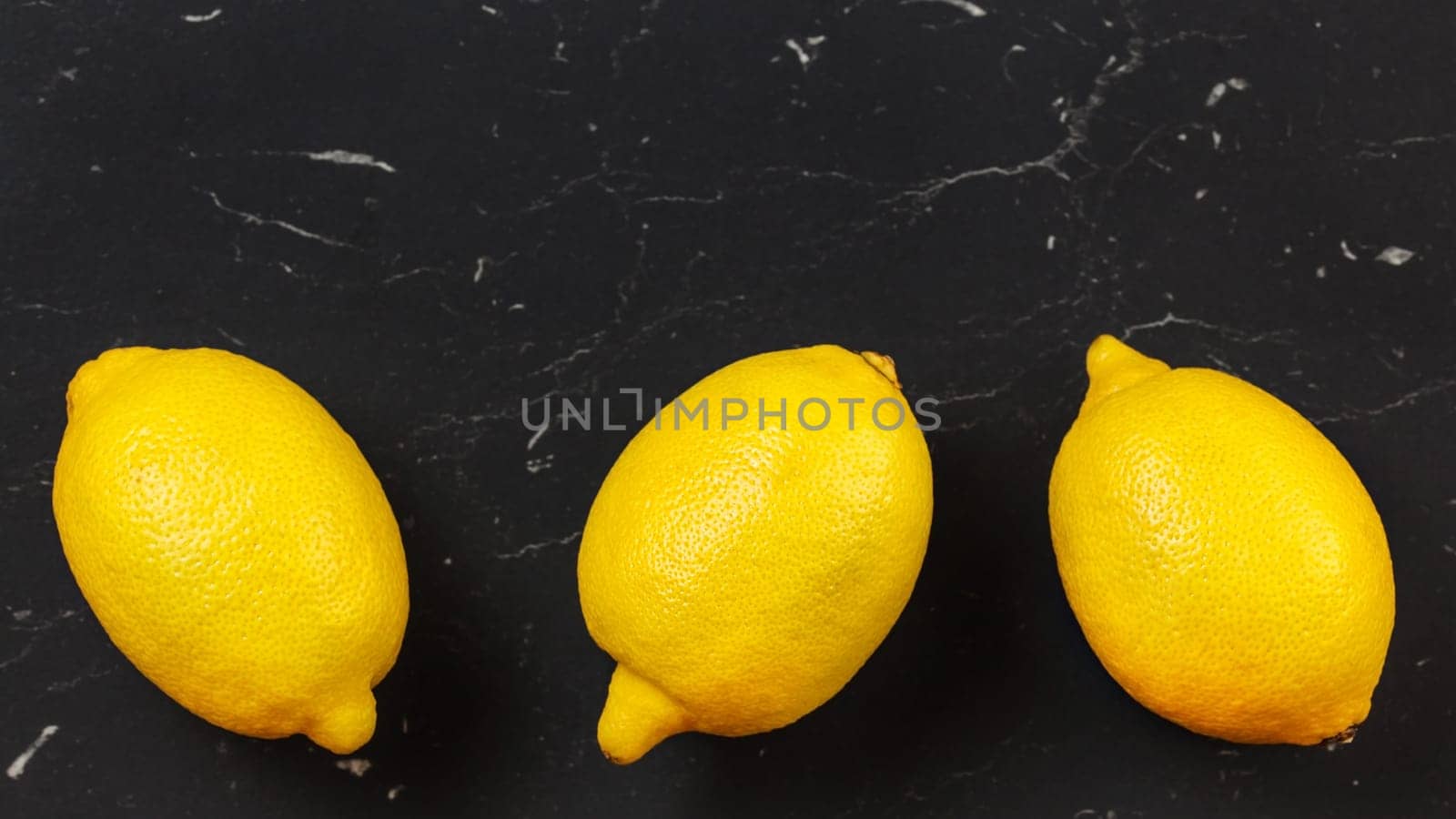 Tabletop view, three whole ripe lemons on black stone board. Space for text above