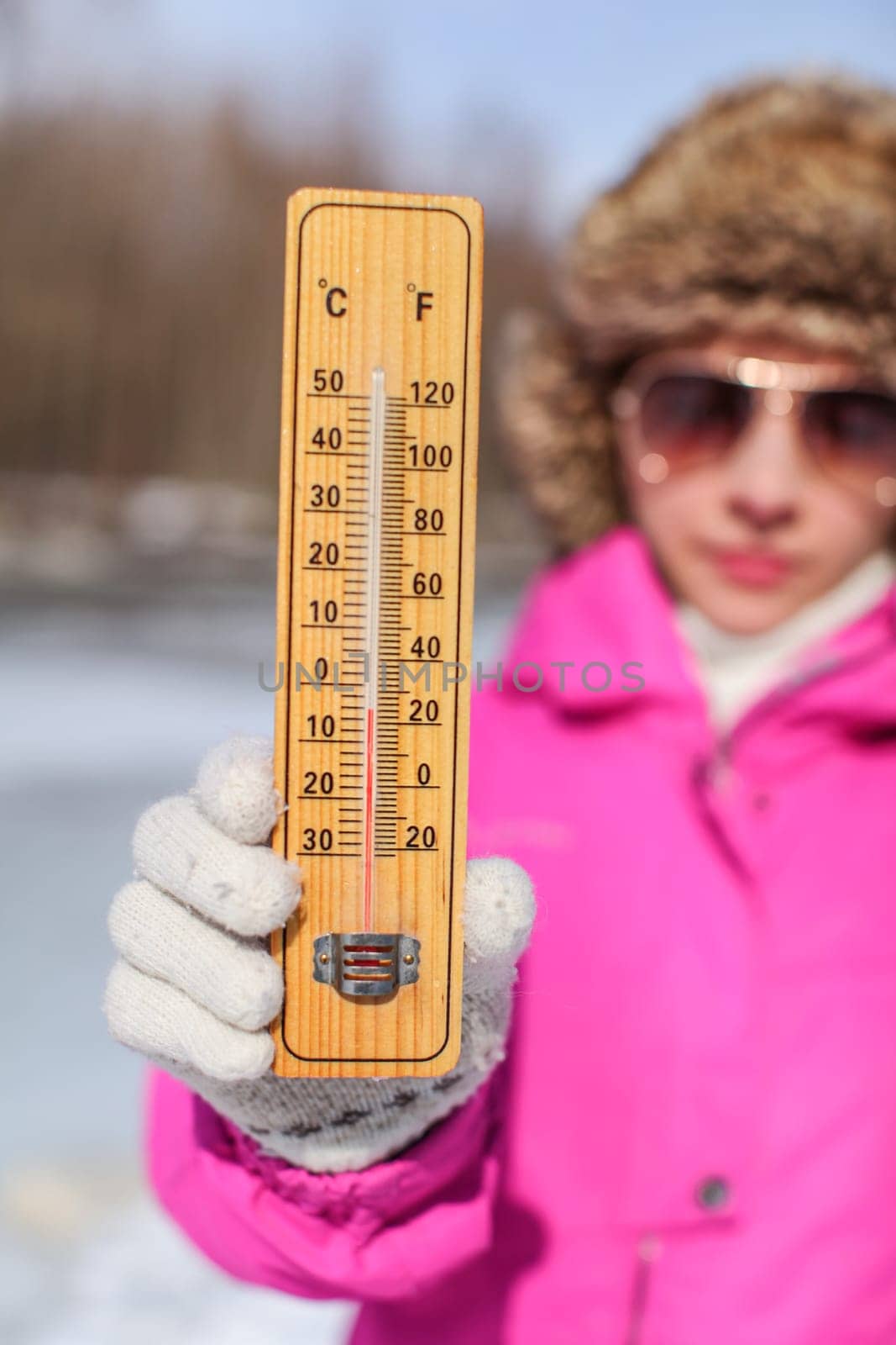 Young woman in pink winter jacked, gloves and furry hat holding thermometer that is showing -5 degrees. Winter / cold days coming concept. by Ivanko