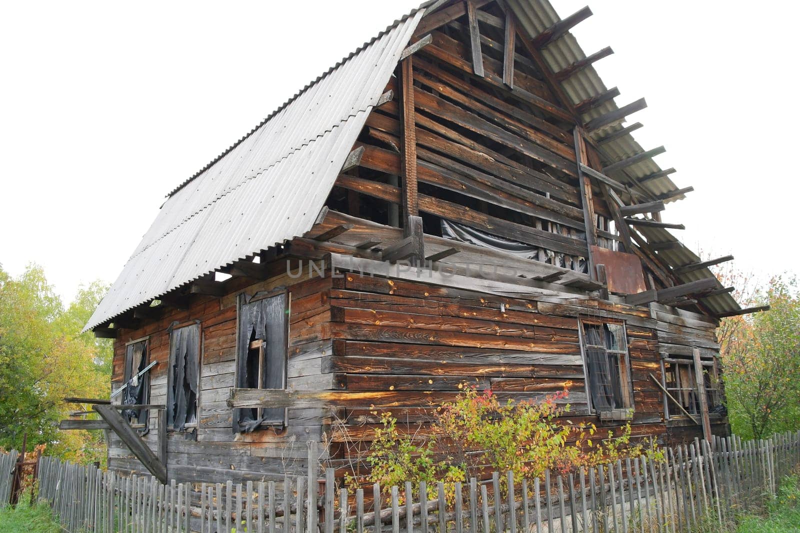 abandoned wooden house with a fence and a garden in the countryside.