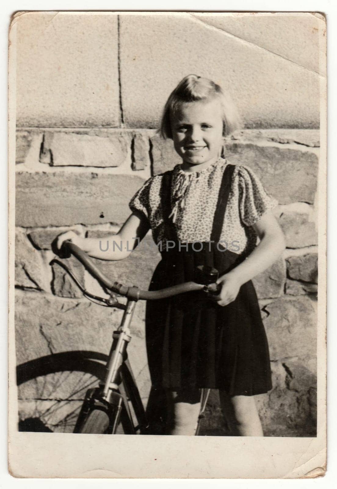 Vintage photo shows a small girl with bicycle. Retro black and white photography. Circa 1950s. by roman_nerud