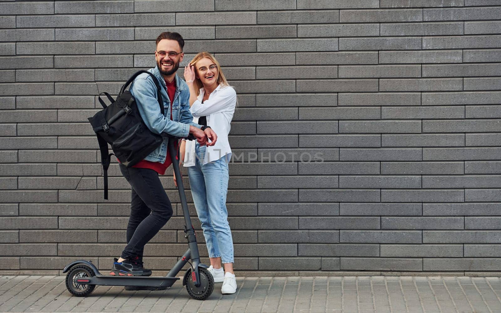 With electric schooter. Young stylish man with woman in casual clothes outdoors together. Conception of friendship or relationships.