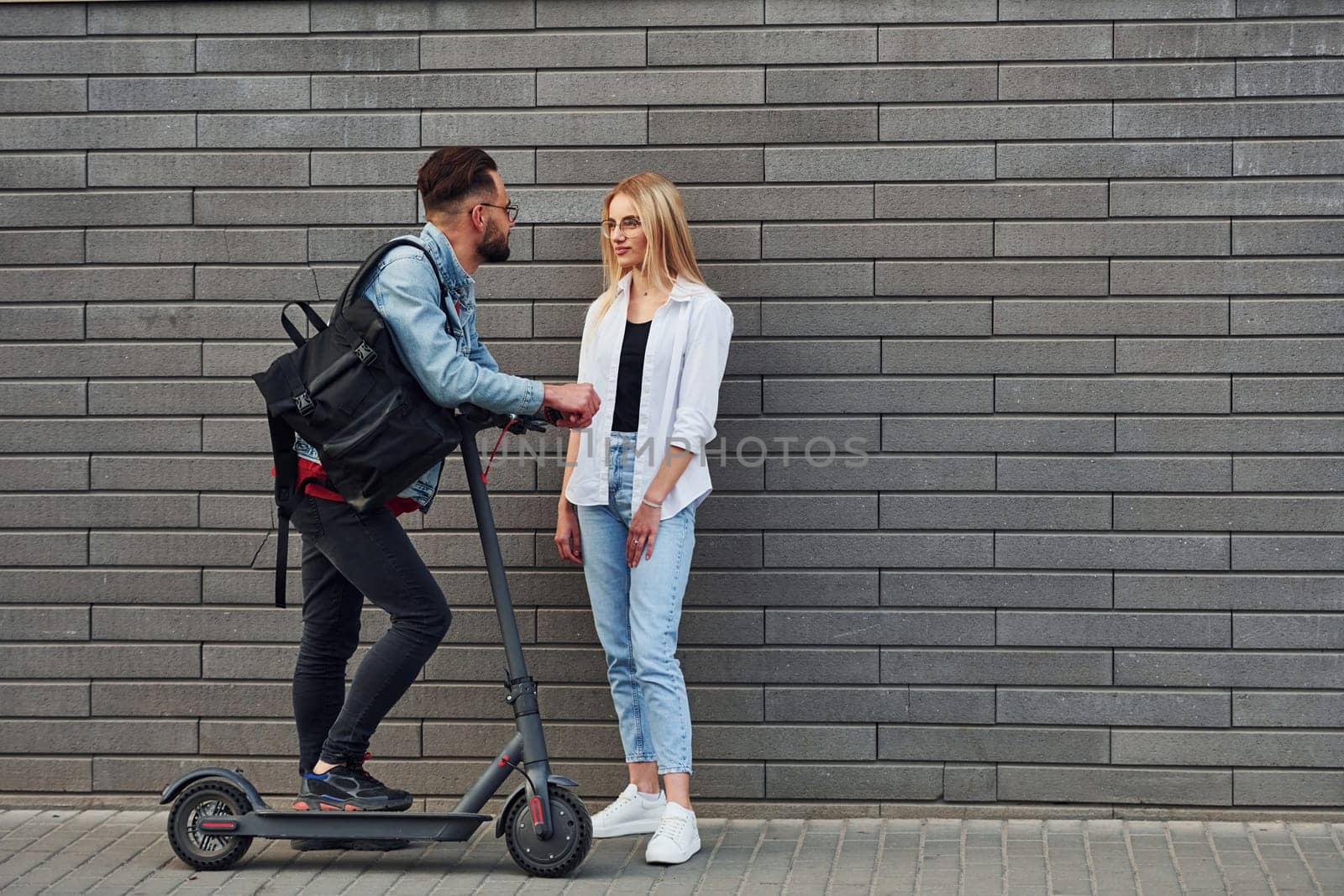 With electric schooter. Young stylish man with woman in casual clothes outdoors together. Conception of friendship or relationships.