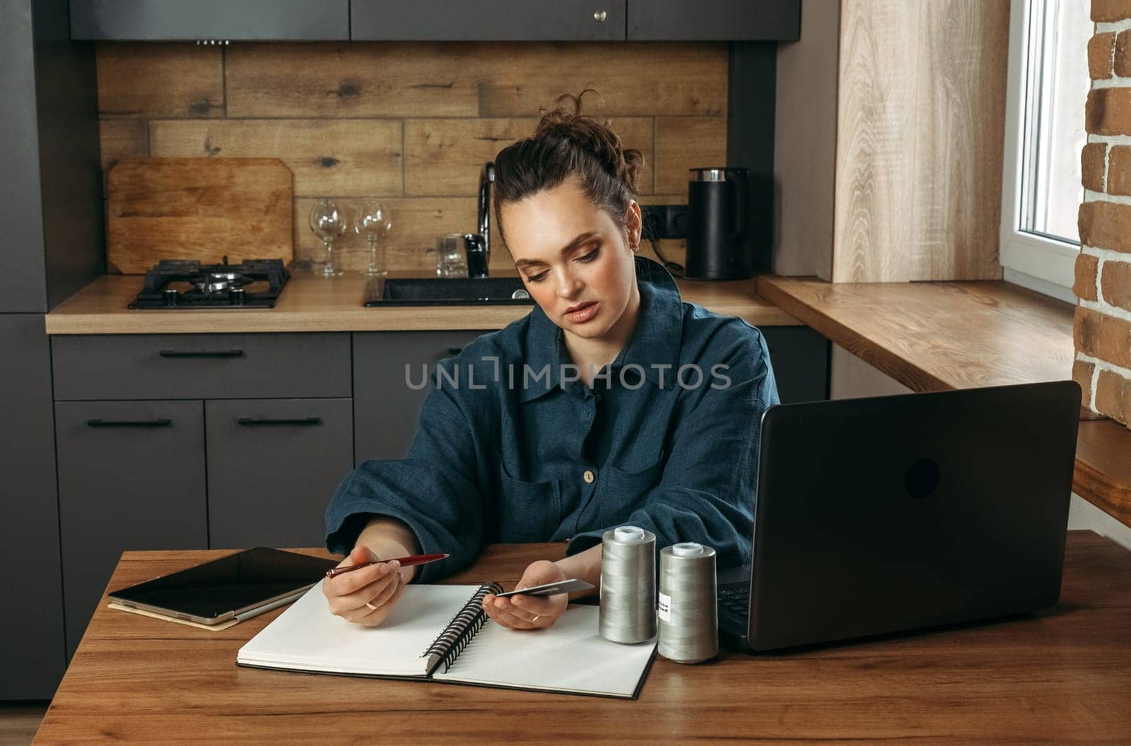 A woman, a clothing designer, makes entries in a diary, works at a computer, tablet.
