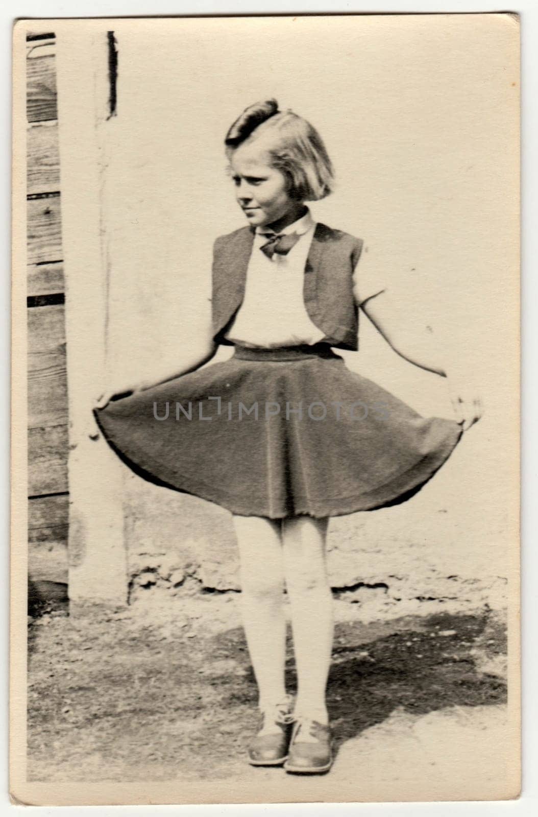 Vintage photo shows a young girl outdoors. She shows her skirt proudly. Retro black and white photography. Circa 1940s. by roman_nerud