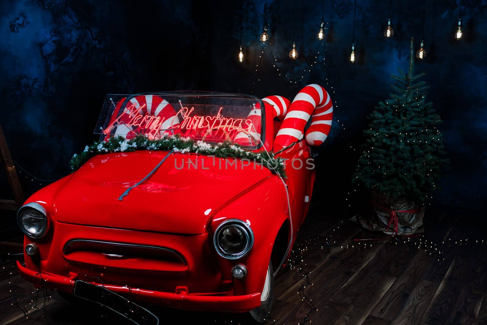 tro red car with led red inscription merry christmas on it. big christmas lollipops in the car in studio background.