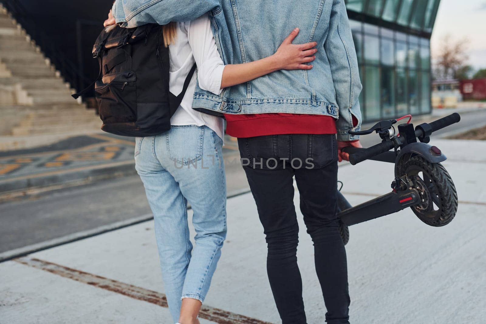 With electric schooter. Young stylish man with woman in casual clothes outdoors near business building together. Conception of friendship or relationships.