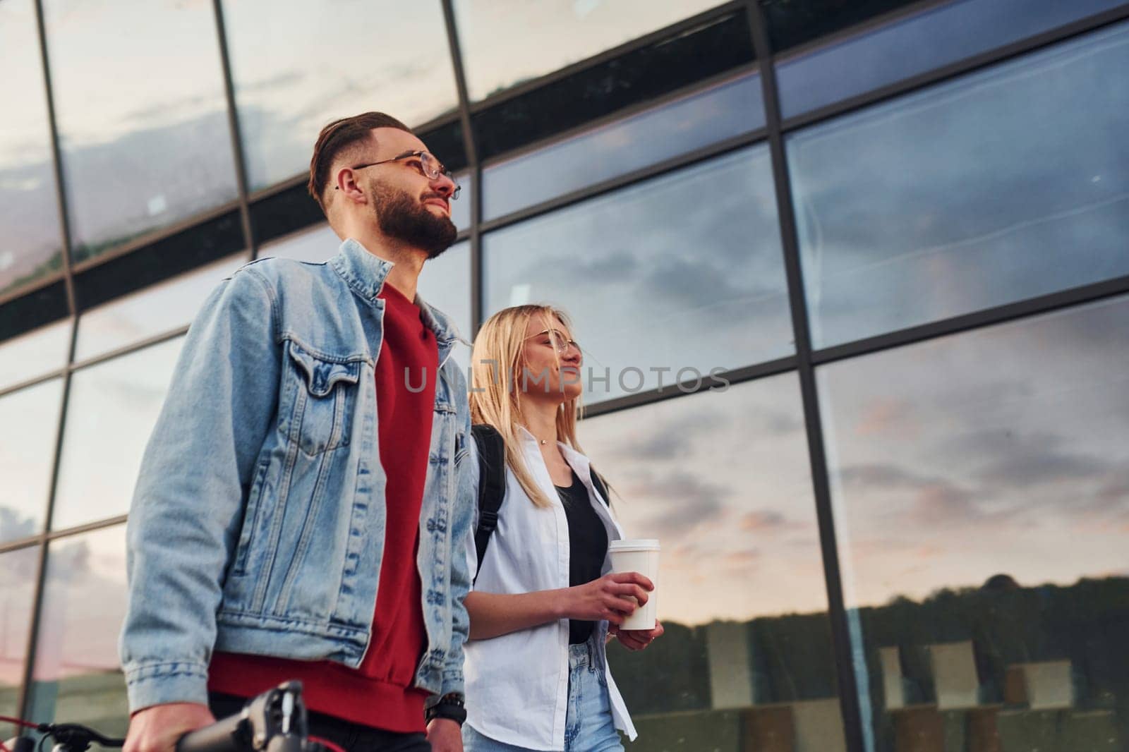 With electric schooter. Young stylish man with woman in casual clothes outdoors near business building together. Conception of friendship or relationships.