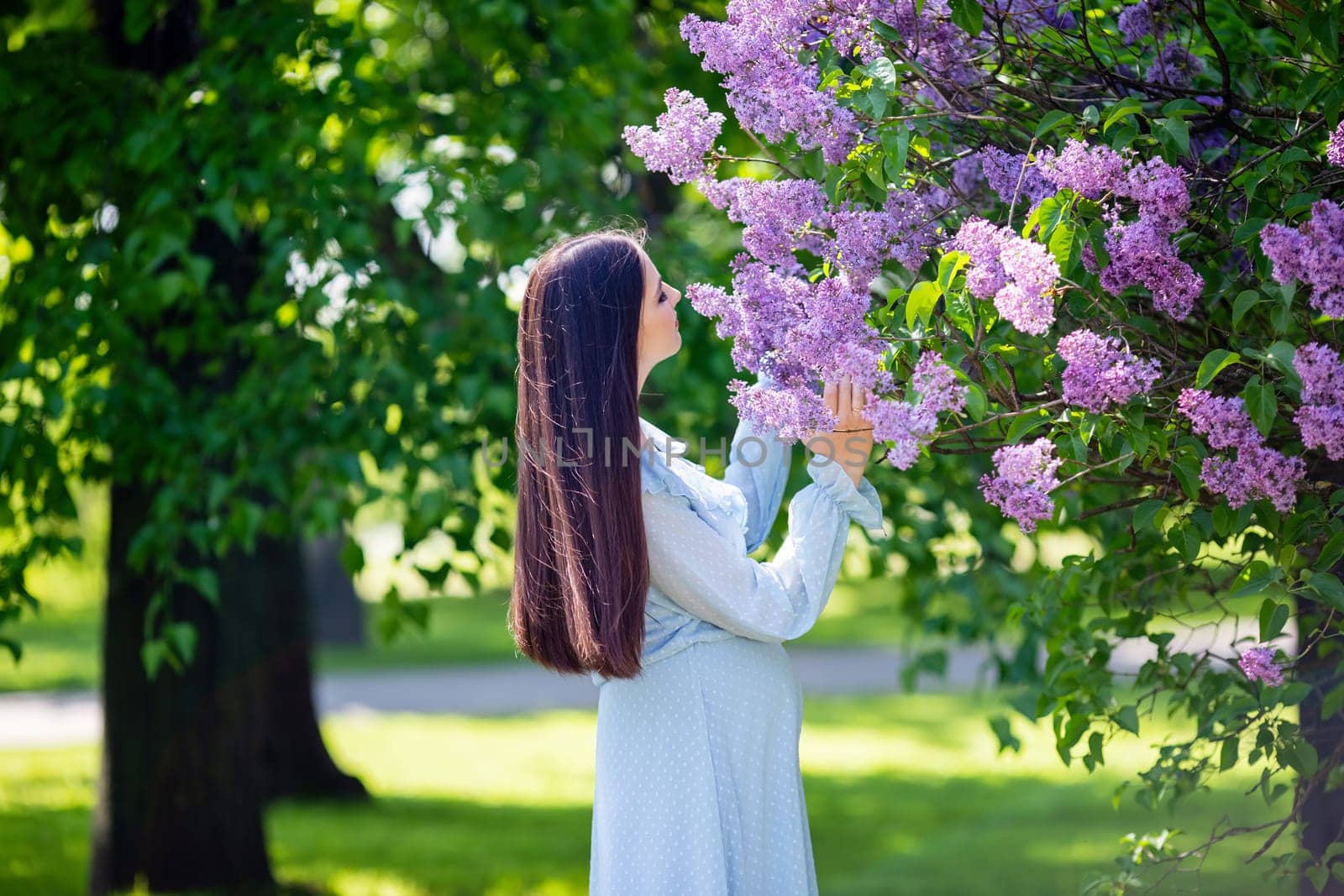 girl with long hair , in light blue dress stands nearby lilac flowers, in the garden, in sunny day. Close up. copy space