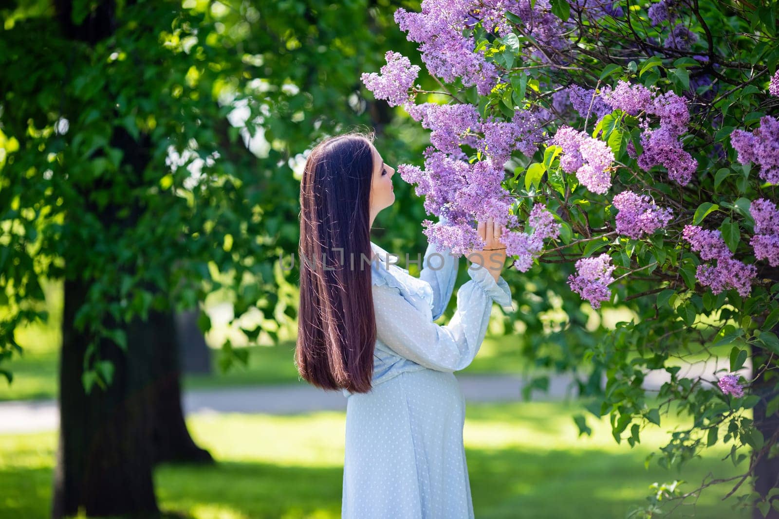 girl with long hair , in light blue dress stands nearby lilac flowers, in the garden, in sunny day. Close up. copy space