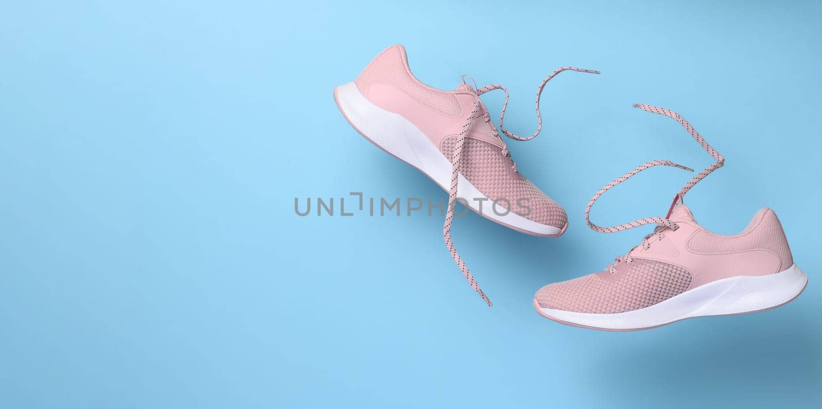 Pink women's sports sneakers with laces levitate on a blue background by ndanko