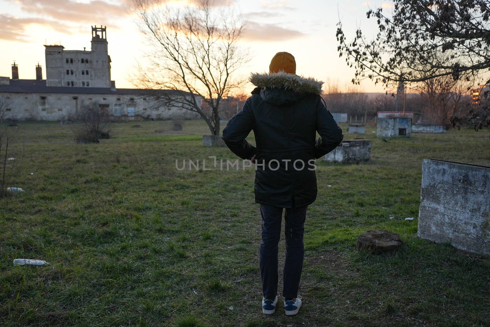 Slender tall man standing looking at an abandoned building in winter sunset. High quality photo