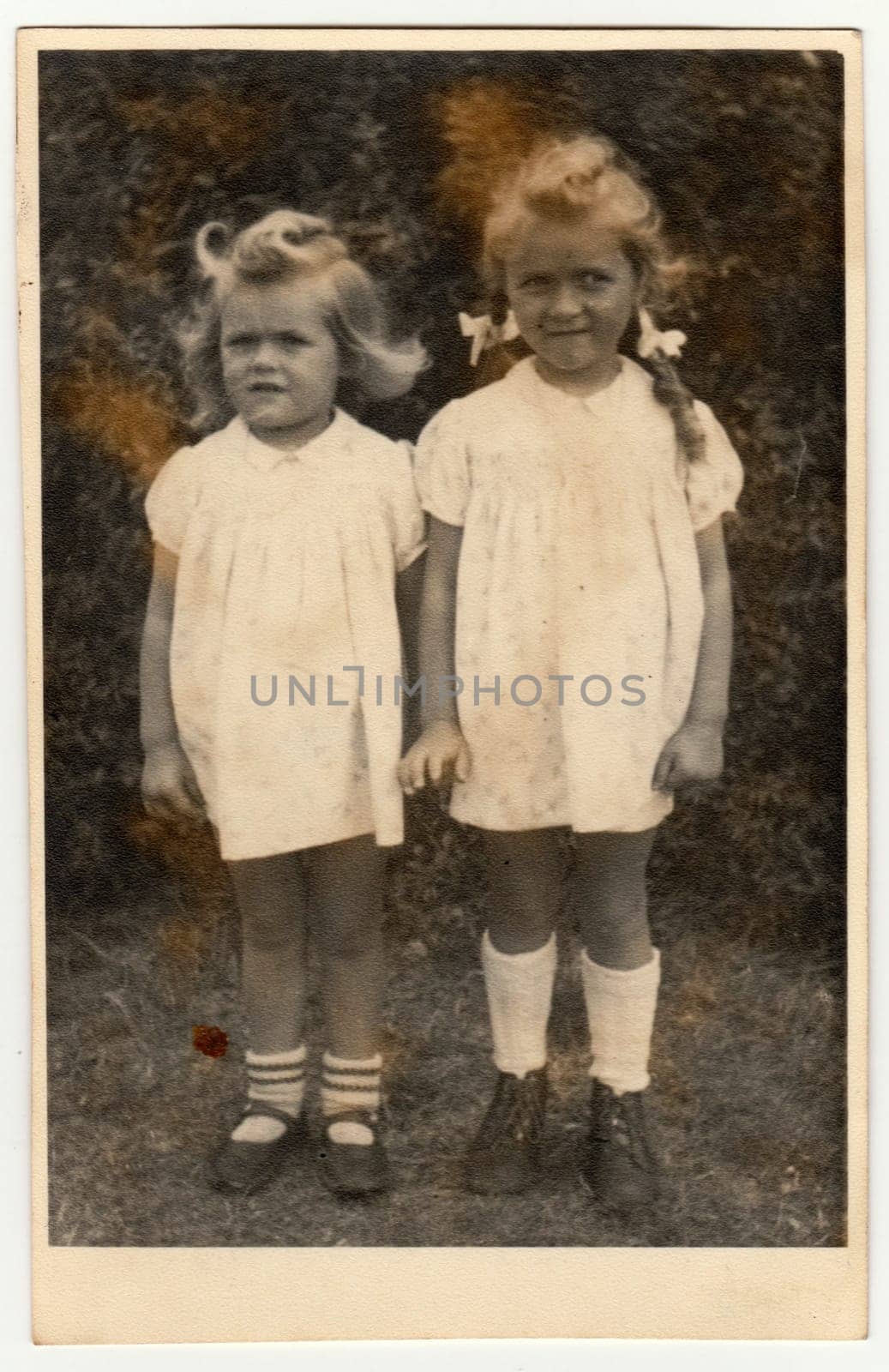 Vintage photo shows two small girls - siblings. They wear a white dresses. Retro black and white photography. Circa 1940s by roman_nerud