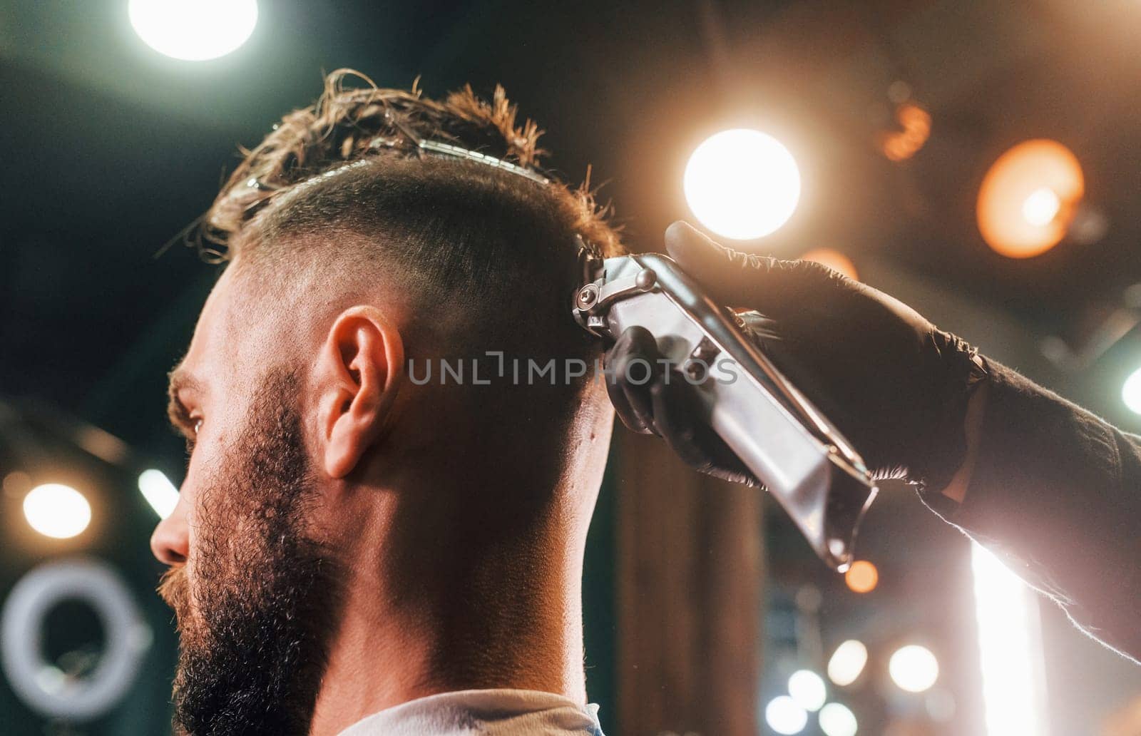 Close up view of young bearded man that sitting and getting haircut in barber shop.