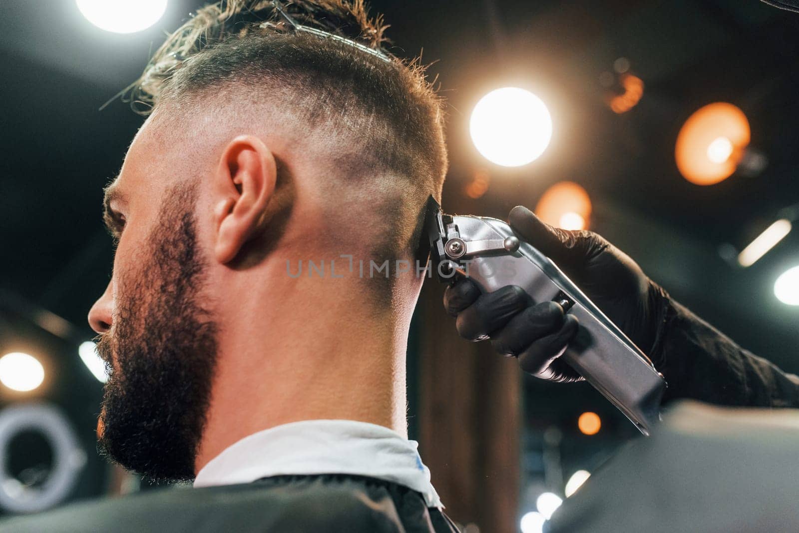 Close up view of young bearded man that sitting and getting haircut in barber shop.