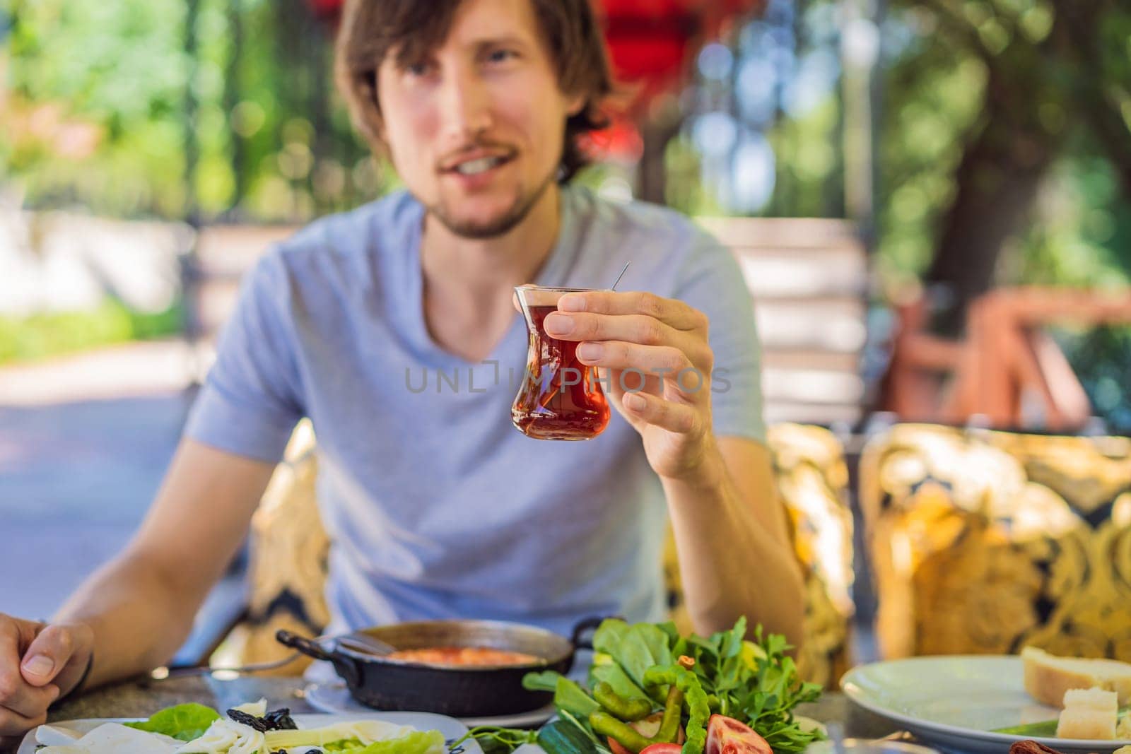 man tourist eat Turkish breakfast. Turkish breakfast table. Pastries. Vegetables. Olives. Cheeses, fried eggs. Jams, tea in copper pot and tulip glasses. Wide composition.