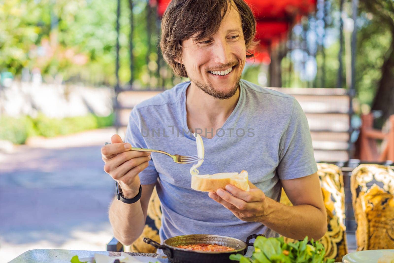 man tourist eat Turkish breakfast. Turkish breakfast table. Pastries. Vegetables. Olives. Cheeses, fried eggs. Jams, tea in copper pot and tulip glasses. Wide composition.