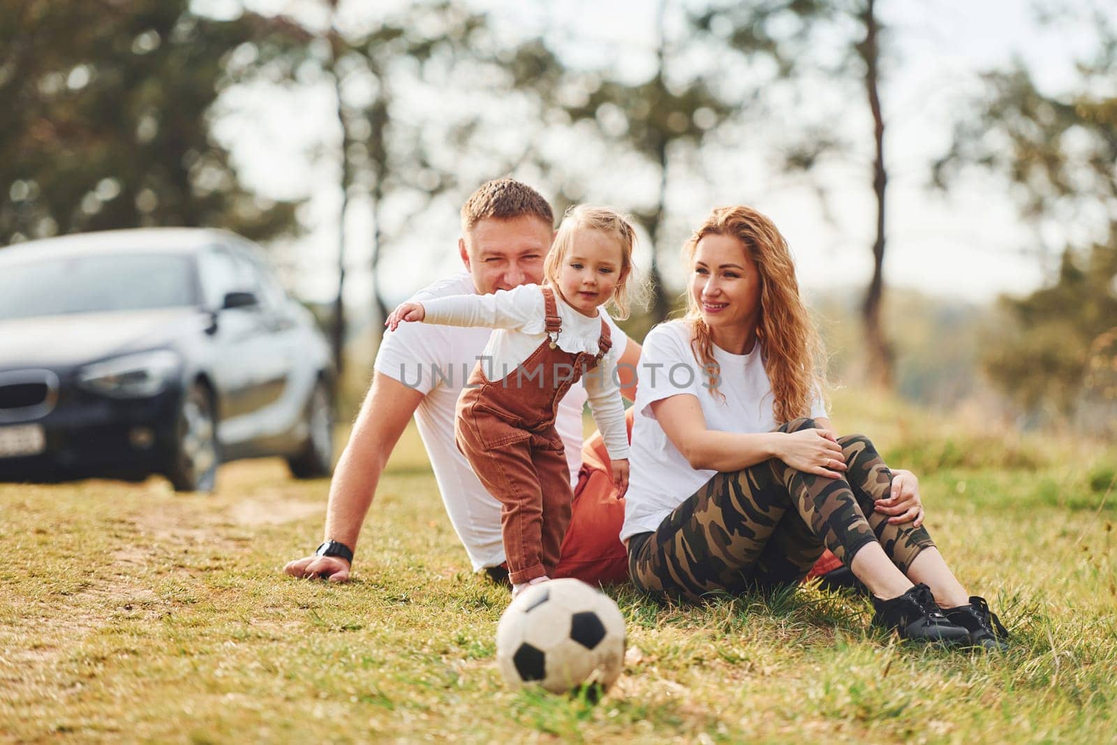 Playing with soccer ball. Father and mother spending weekend outdoors near forest with daughter.