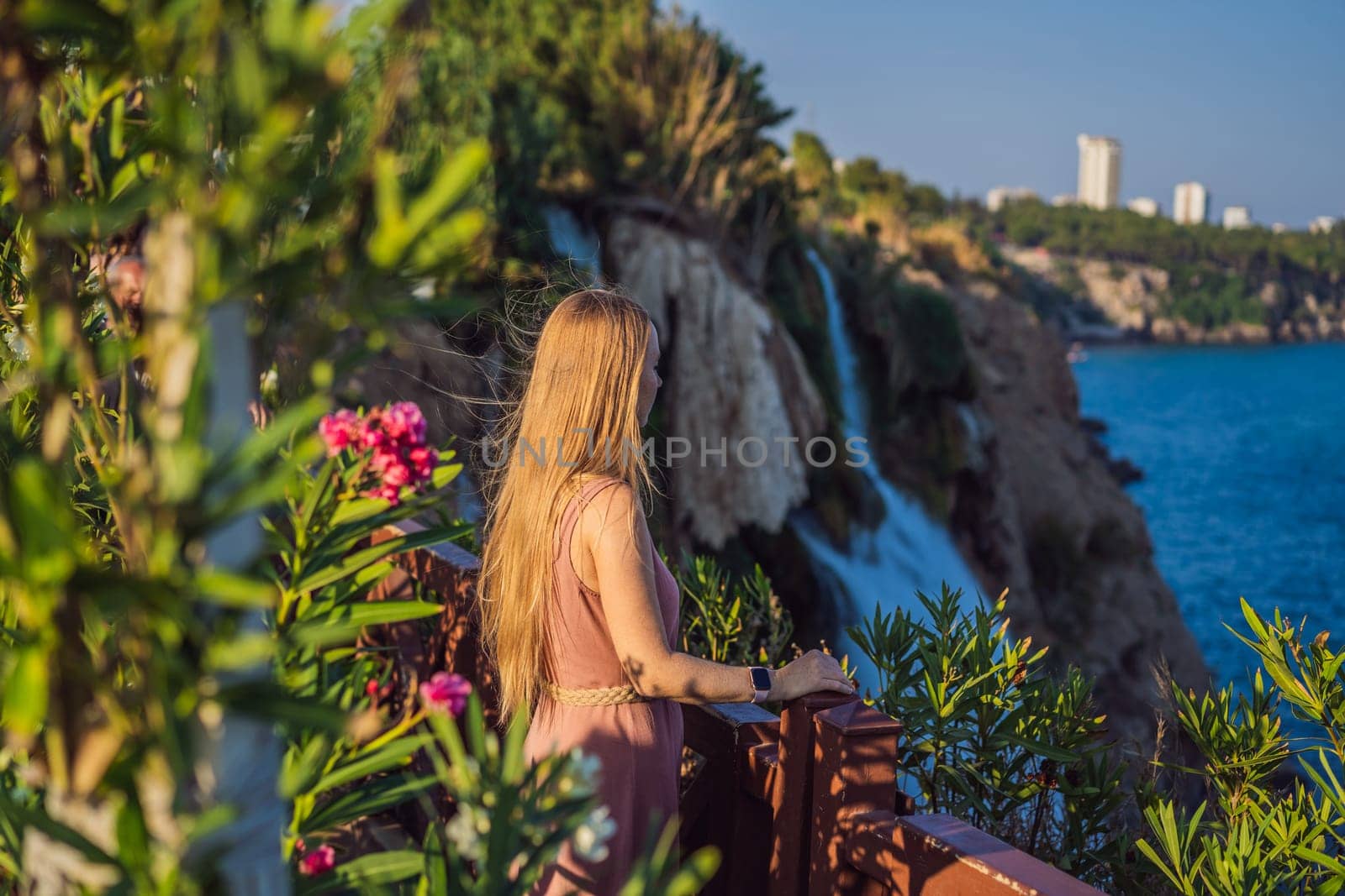 Beautiful woman with long hair on the background of Duden waterfall in Antalya. Famous places of Turkey. Lower Duden Falls drop off a rocky cliff falling from about 40 m into the Mediterranean Sea in amazing water clouds. Tourism and travel destination photo in Antalya, Turkey. Turkiye.