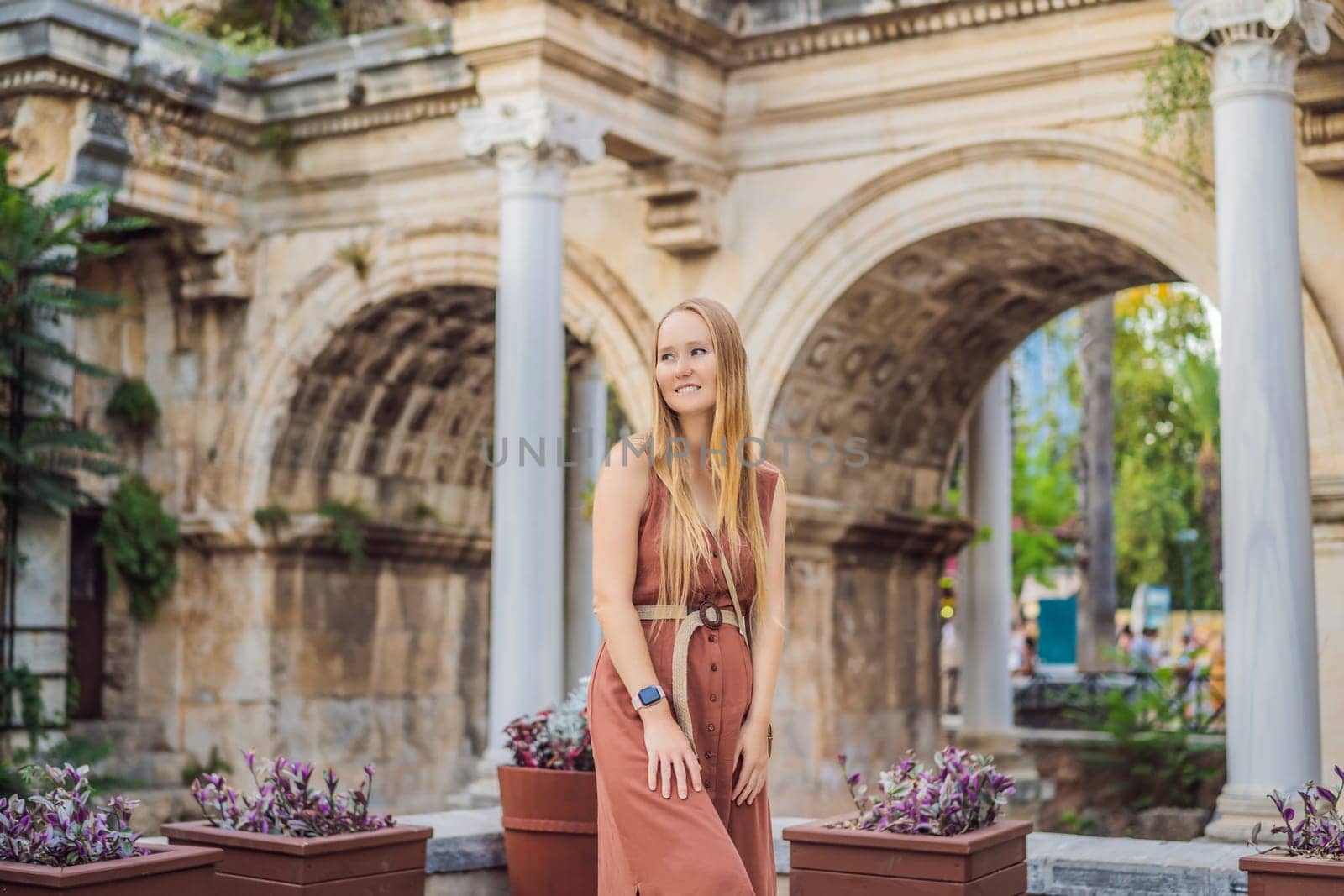 Happy female tourist traveler discover interesting places and popular attractions and walks in the old city of Antalya. Hadrian Kapisi turkey landmark city history. Popular tourist attraction - ancient Roman Hadrian Gate in old town Antalya, Turkey on a summer day. Turkiye.