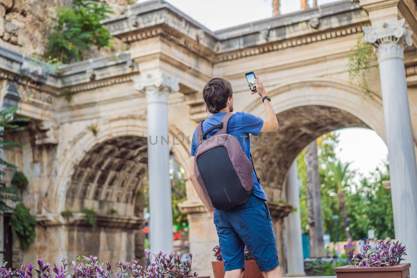 Happy male tourist traveler discover interesting places and popular attractions and walks in the old city of Antalya. Hadrian Kapisi turkey landmark city history. Popular tourist attraction - ancient Roman Hadrian Gate in old town Antalya, Turkey on a summer day. Turkiye.