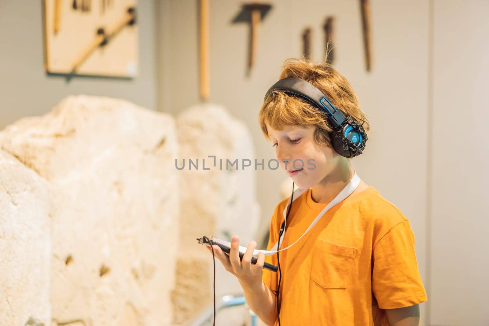 Boy looking at sculptures and listening to audio guide at museum exhibition.
