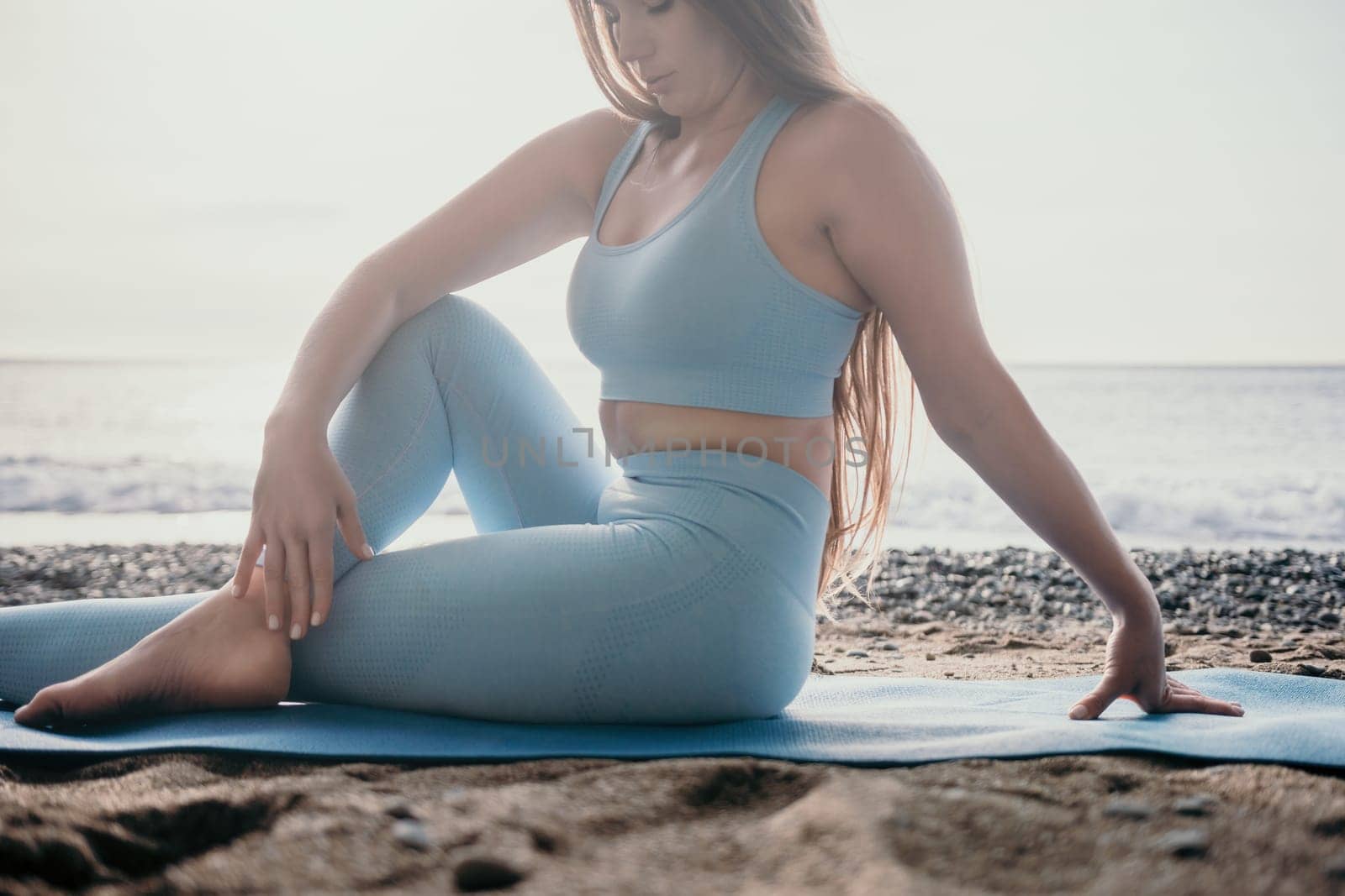 Middle aged well looking woman with black hair doing Pilates with the ring on the yoga mat near the sea on the pebble beach. Female fitness yoga concept. Healthy lifestyle, harmony and meditation.