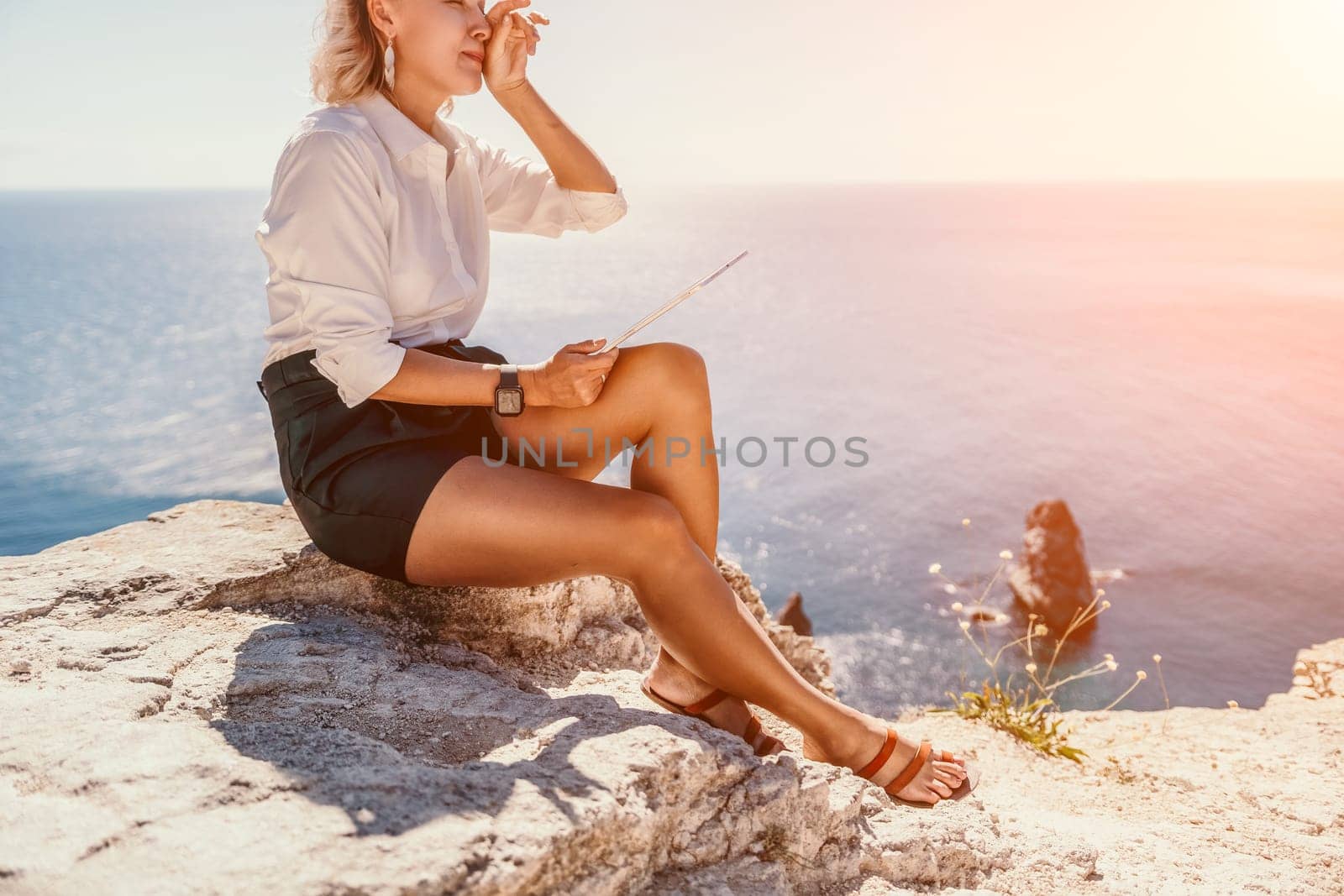 Successful business woman in yellow hat working on laptop by the sea. Pretty lady typing on computer at summer day outdoors. Freelance, travel and holidays concept.