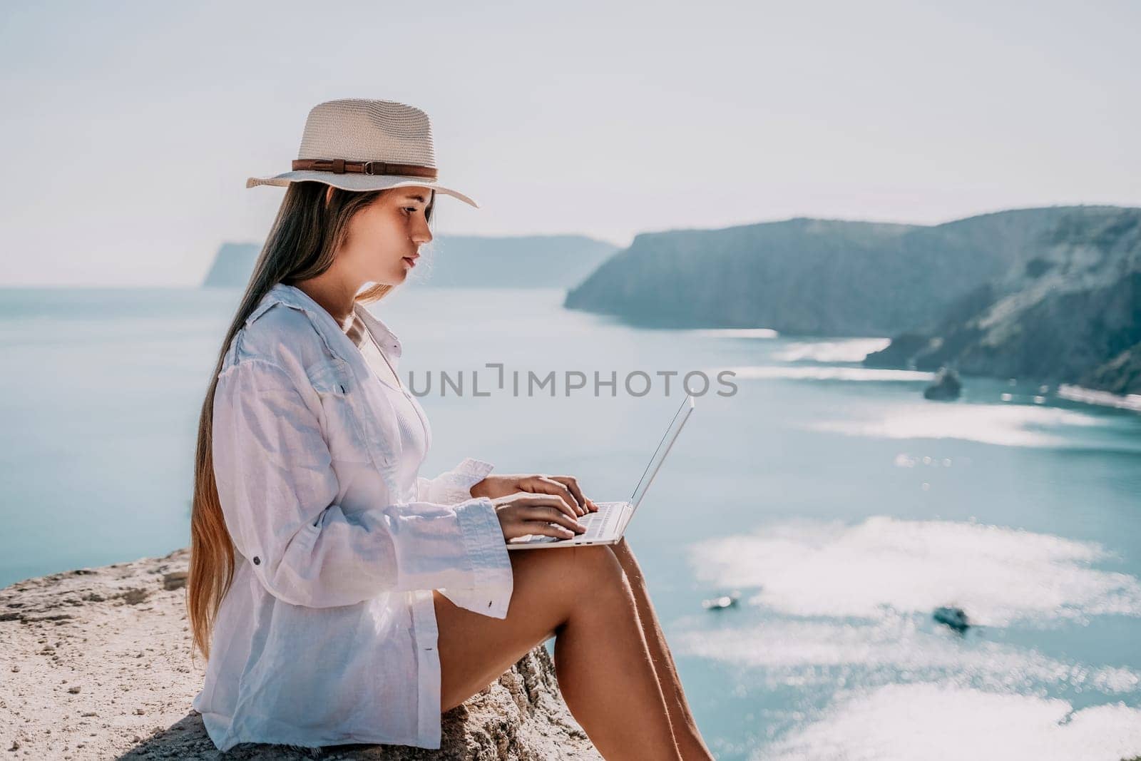 Woman sea laptop. Business woman in yellow hat freelancer with laptop working over blue sea beach. Girl relieves stress from work. Freelance, digital nomad, travel and holidays concept by panophotograph